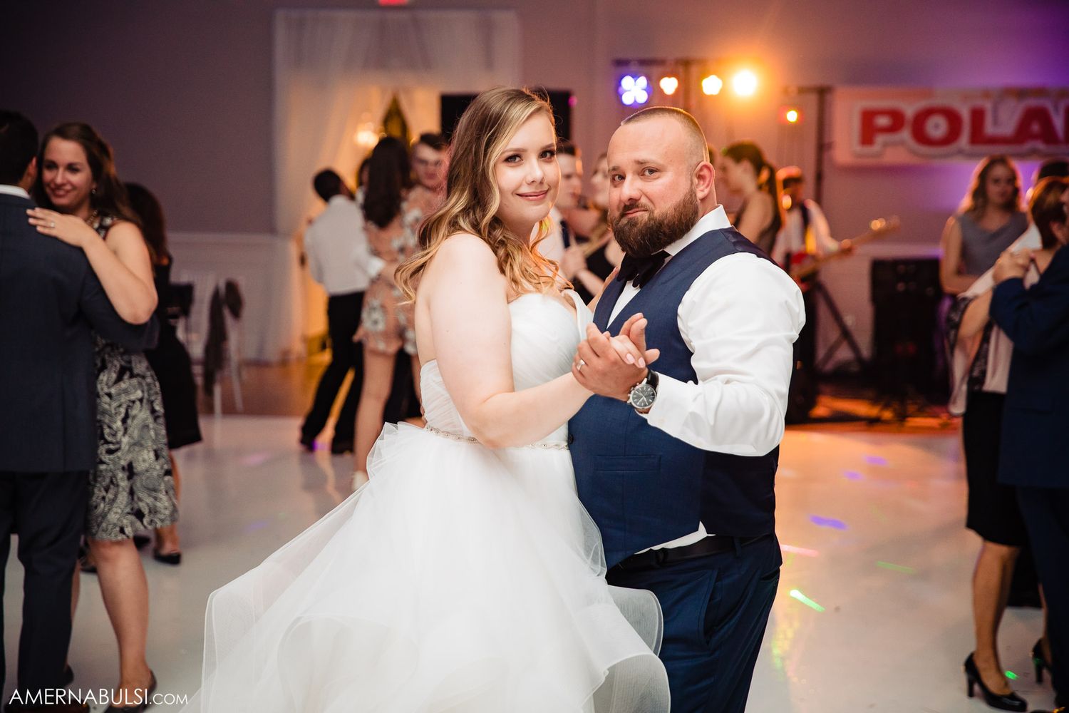A couple shares a romantic dance at their wedding reception with colorful lights illuminating the dance floor.