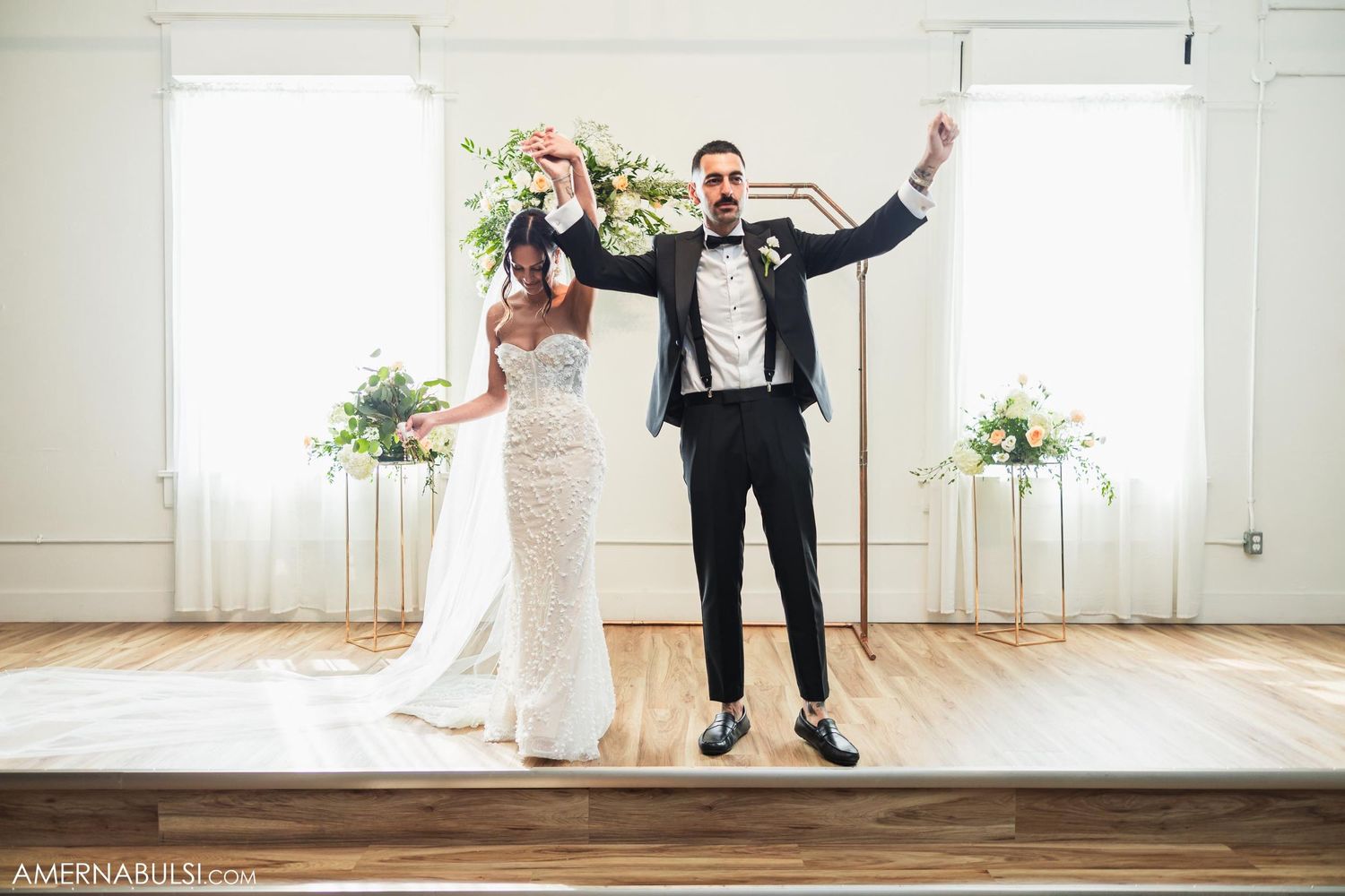 Joyful wedding couple celebrates with energetic pose on wooden floor.