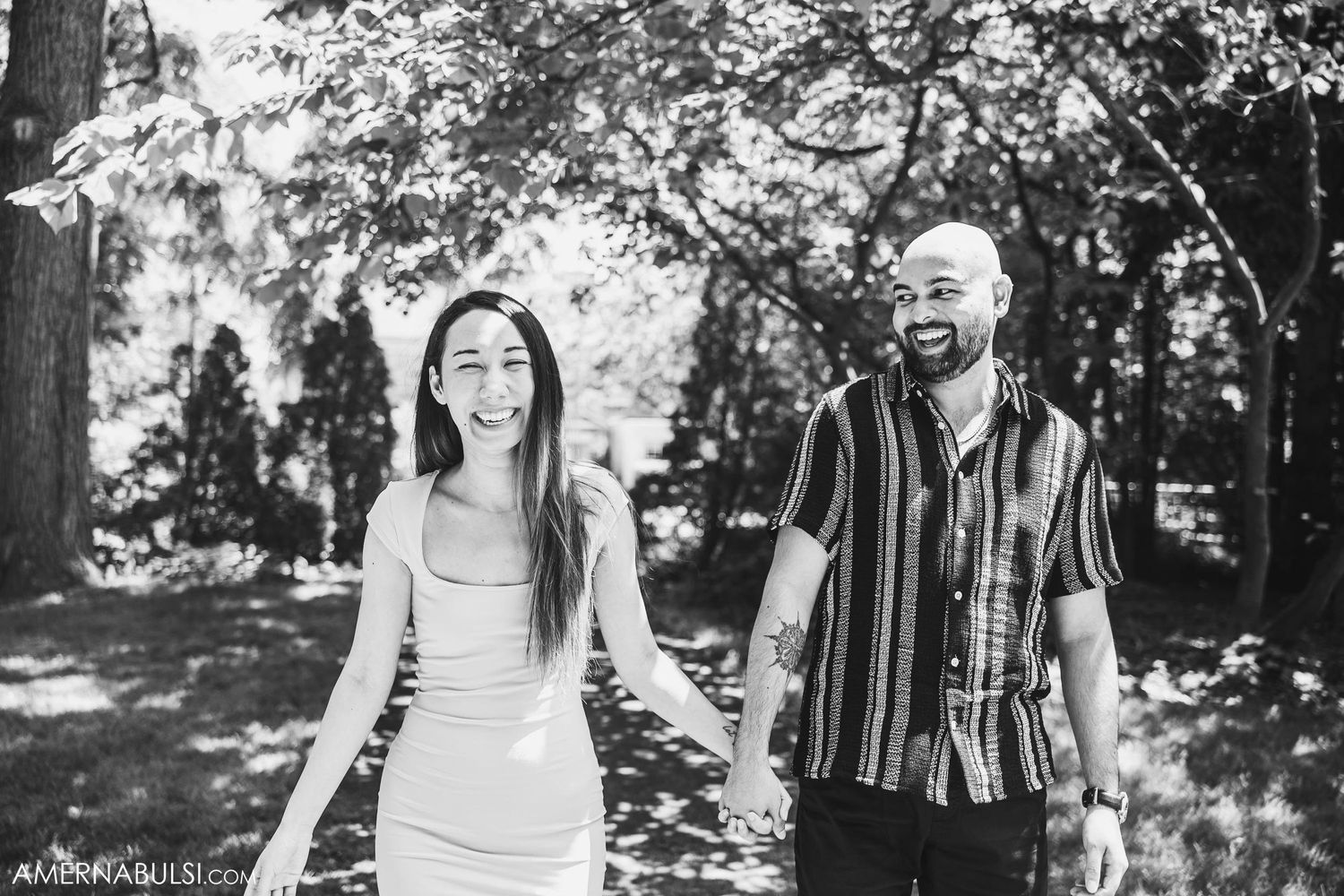 A black and white photo of a couple laughing together in a park setting.