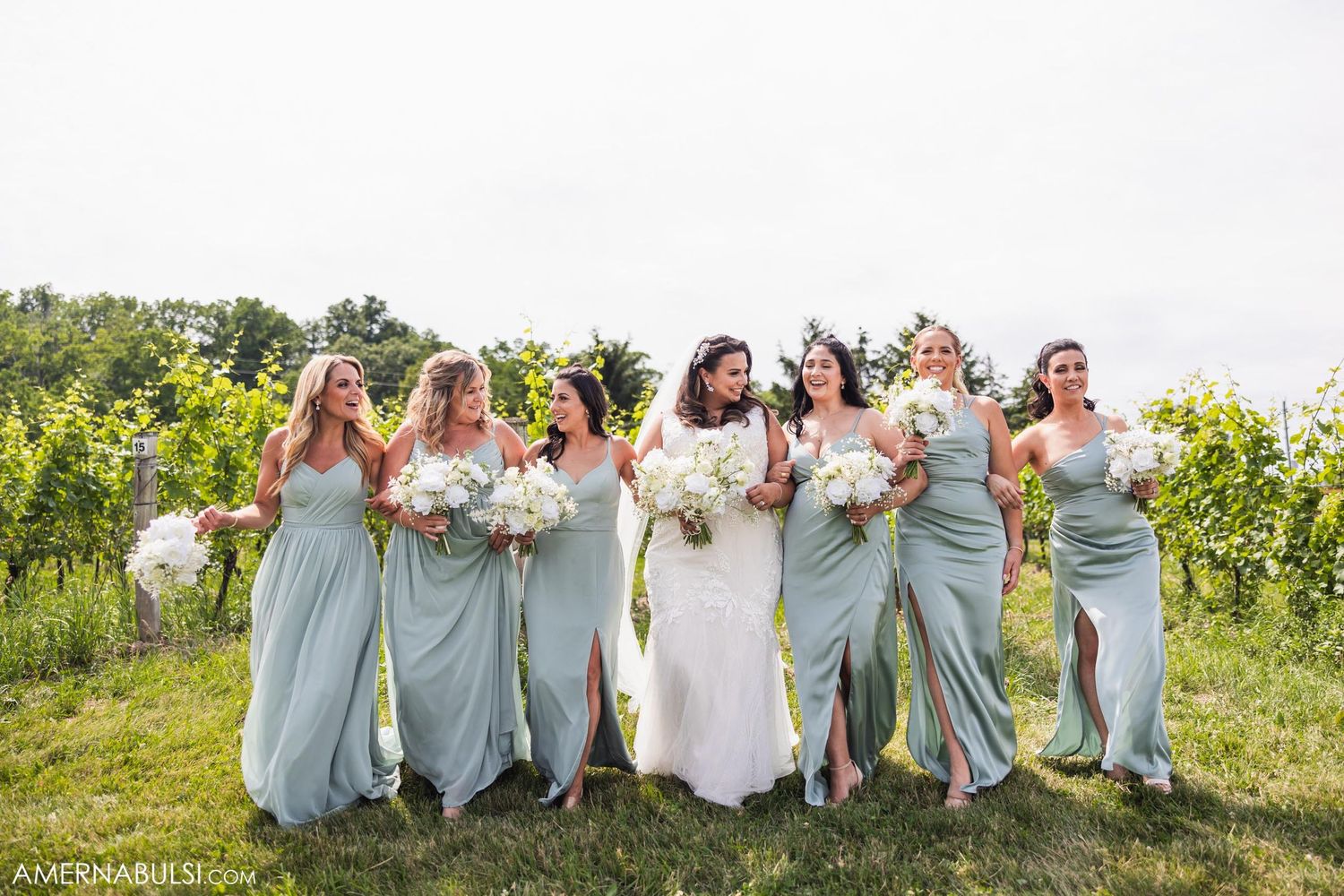 Bridesmaids in sage green dresses celebrate with bride in vineyard setting.