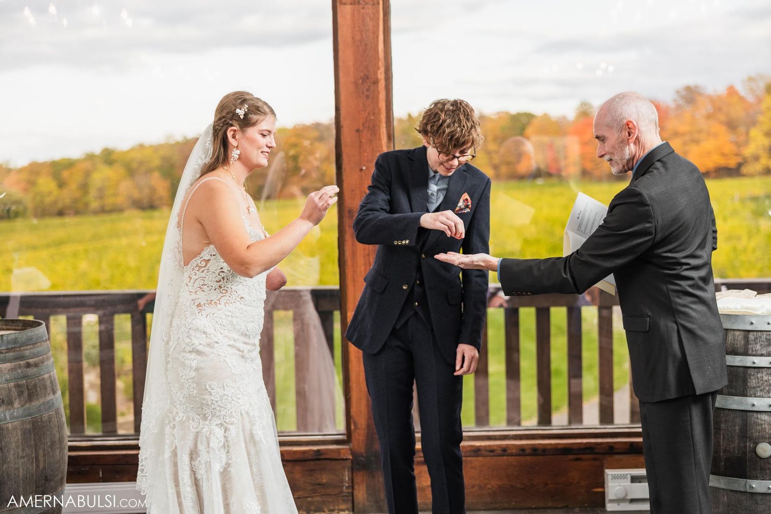 A wedding ceremony takes place on a covered deck overlooking fall foliage.