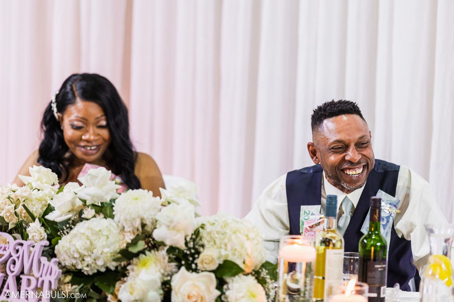A couple shares a joyful moment at their reception table decorated with white hydrangea centerpieces.