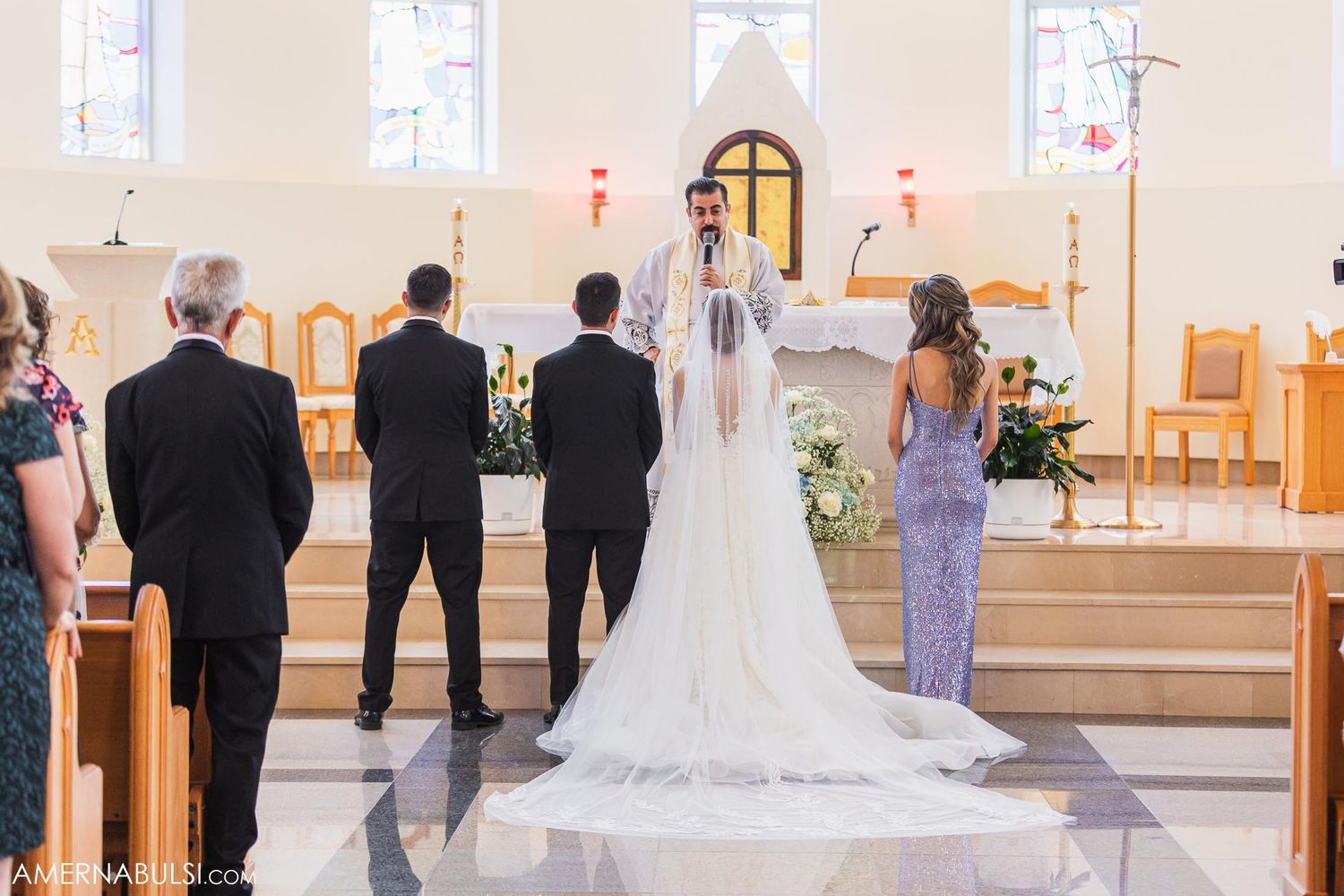 Wedding ceremony participants stand at the church altar under stained glass windows.