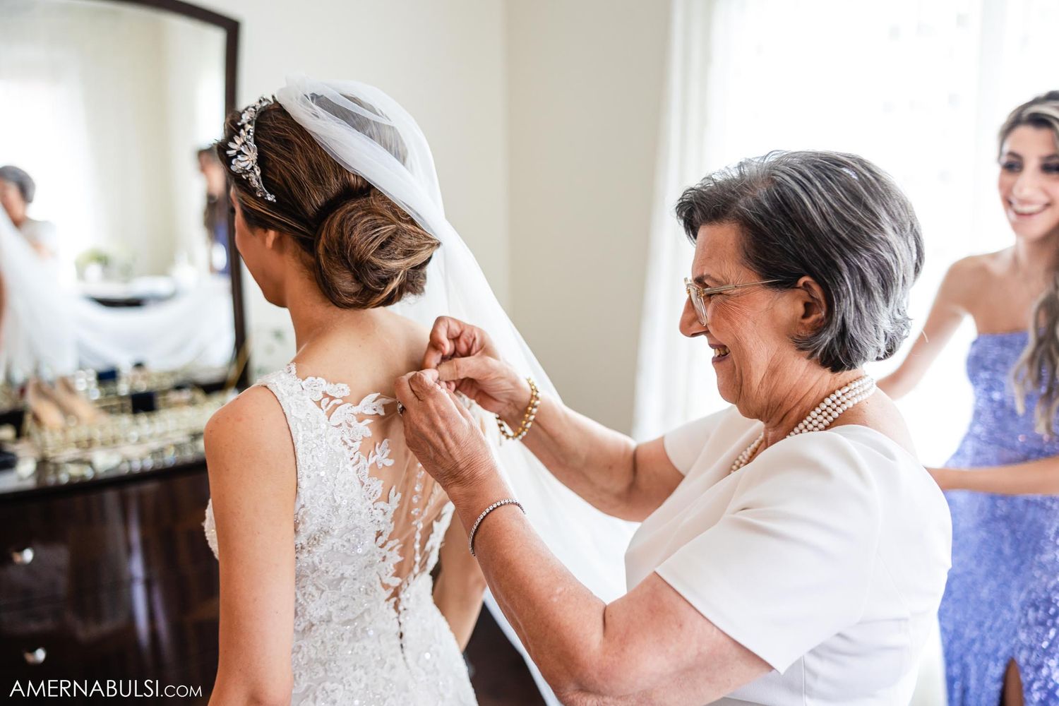 Close-up of detailed lace wedding dress being buttoned up during bridal preparations.