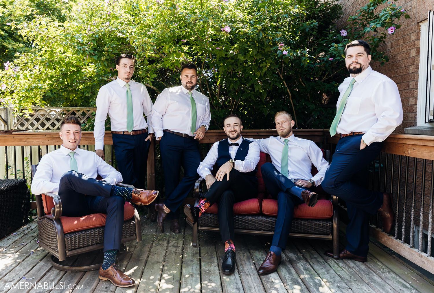 A group of formally dressed people pose together on outdoor furniture on a deck.