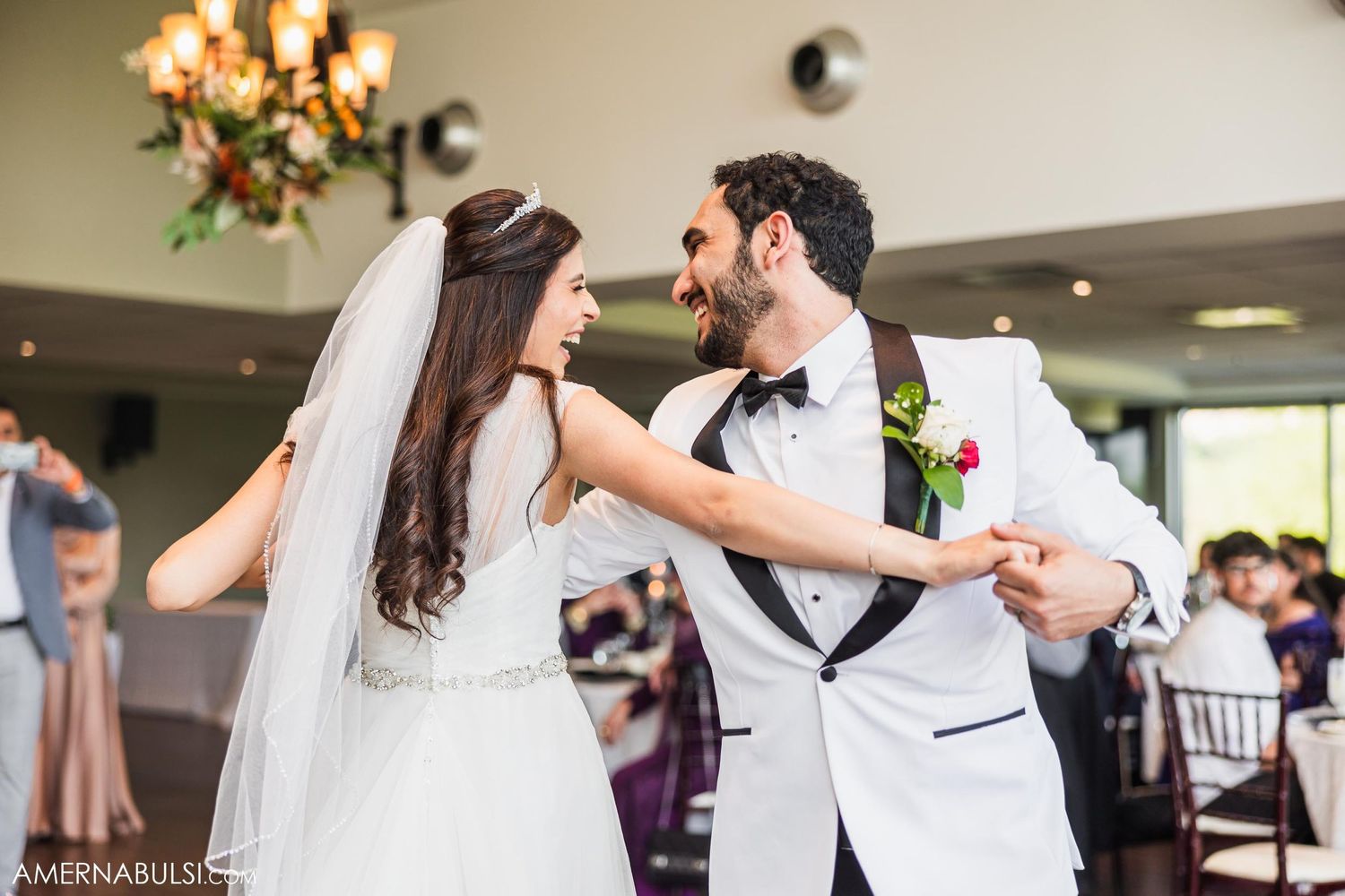 Newlyweds share an intimate dance moment under a chandelier at their reception.
