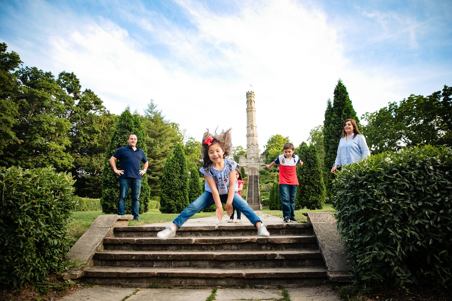 A playful family photo taken in a garden with someone jumping off stone steps while others watch.
