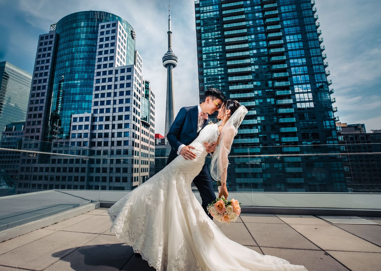 Wedding couple poses against modern city skyline with dramatic architectural backdrop.