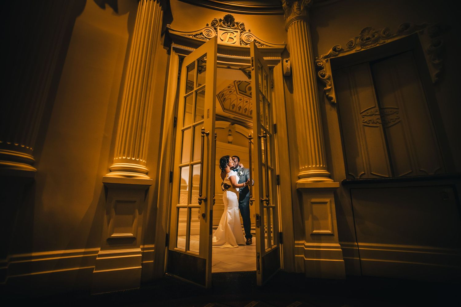 Romantic wedding portrait in an ornate golden doorway with dramatic lighting.