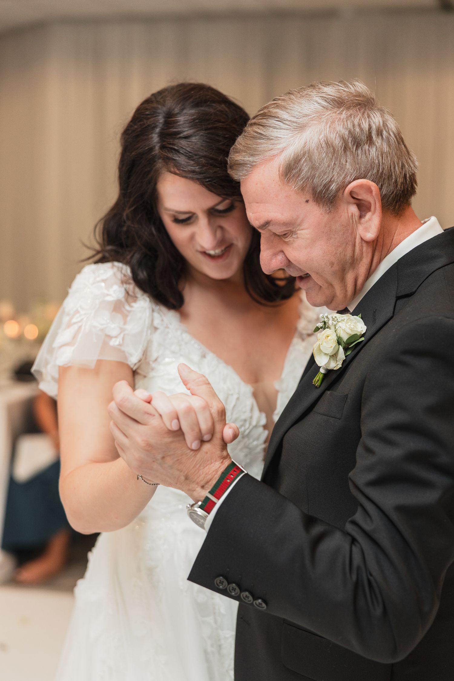 Bride and father share an emotional first dance, holding hands and smiling during wedding reception.