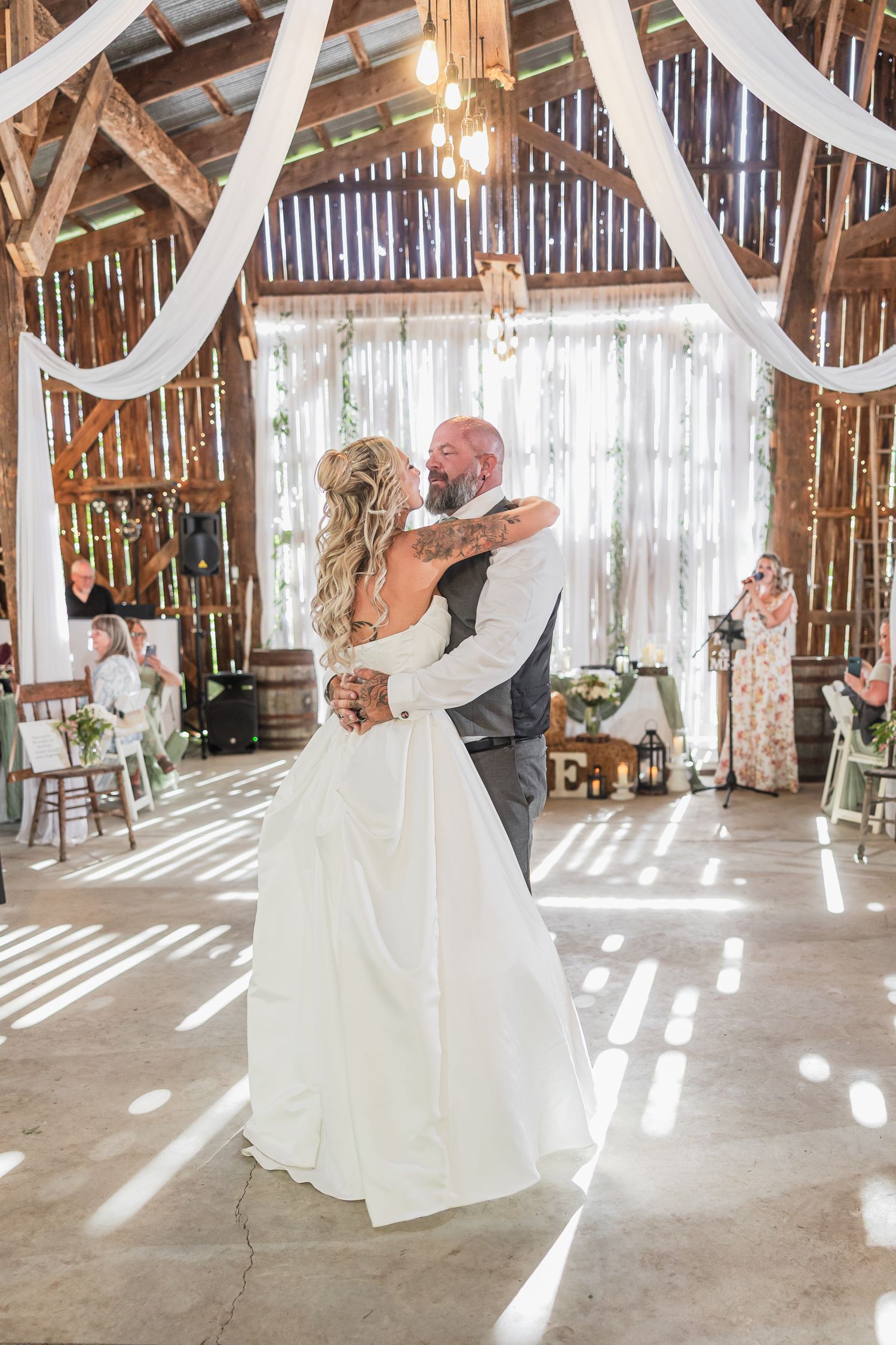 A bride and groom share their first dance in a beautifully decorated rustic barn wedding venue with draped white fabric.