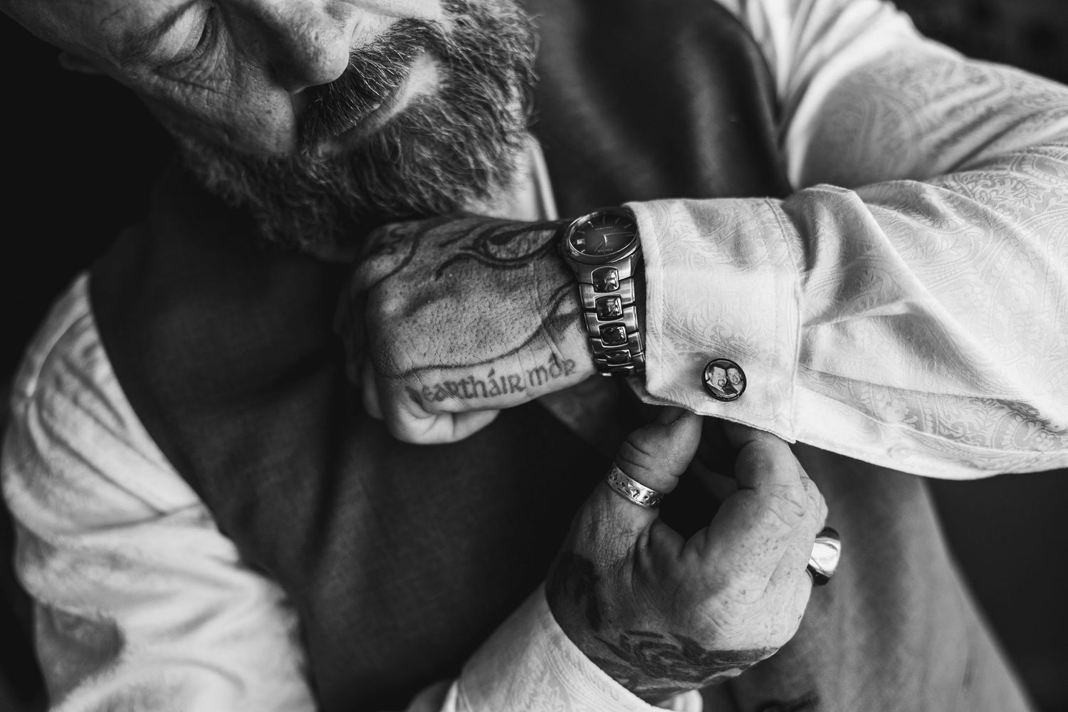 A tattooed man fastens his cufflinks while dressing in a formal white shirt for a special event.