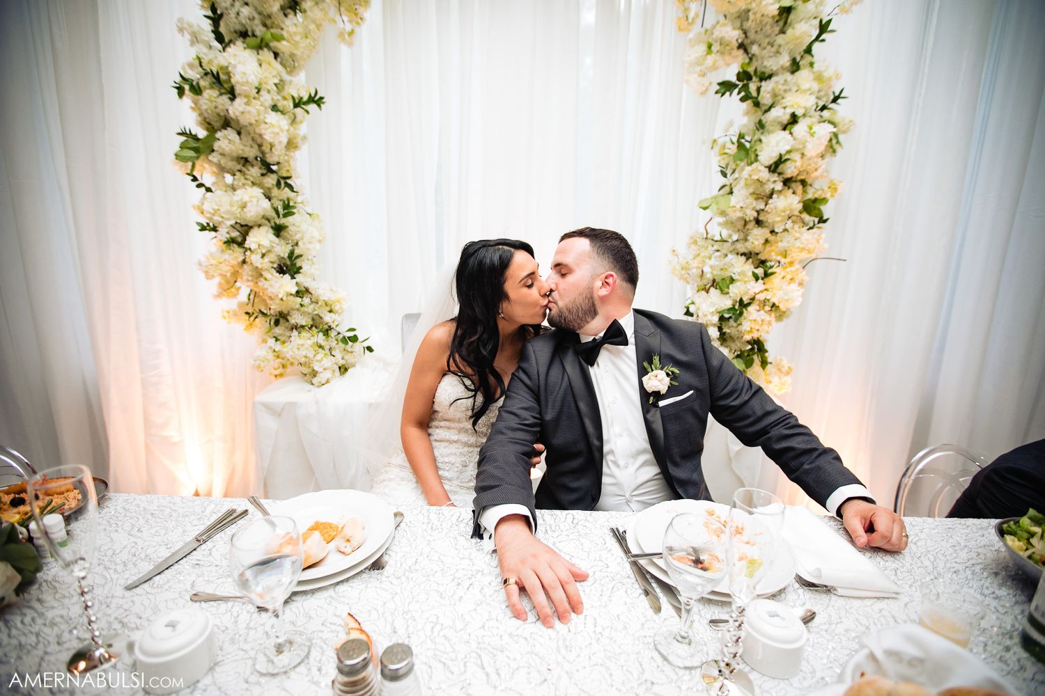 Elegant wedding reception table decorated with white floral arrangements and place settings.