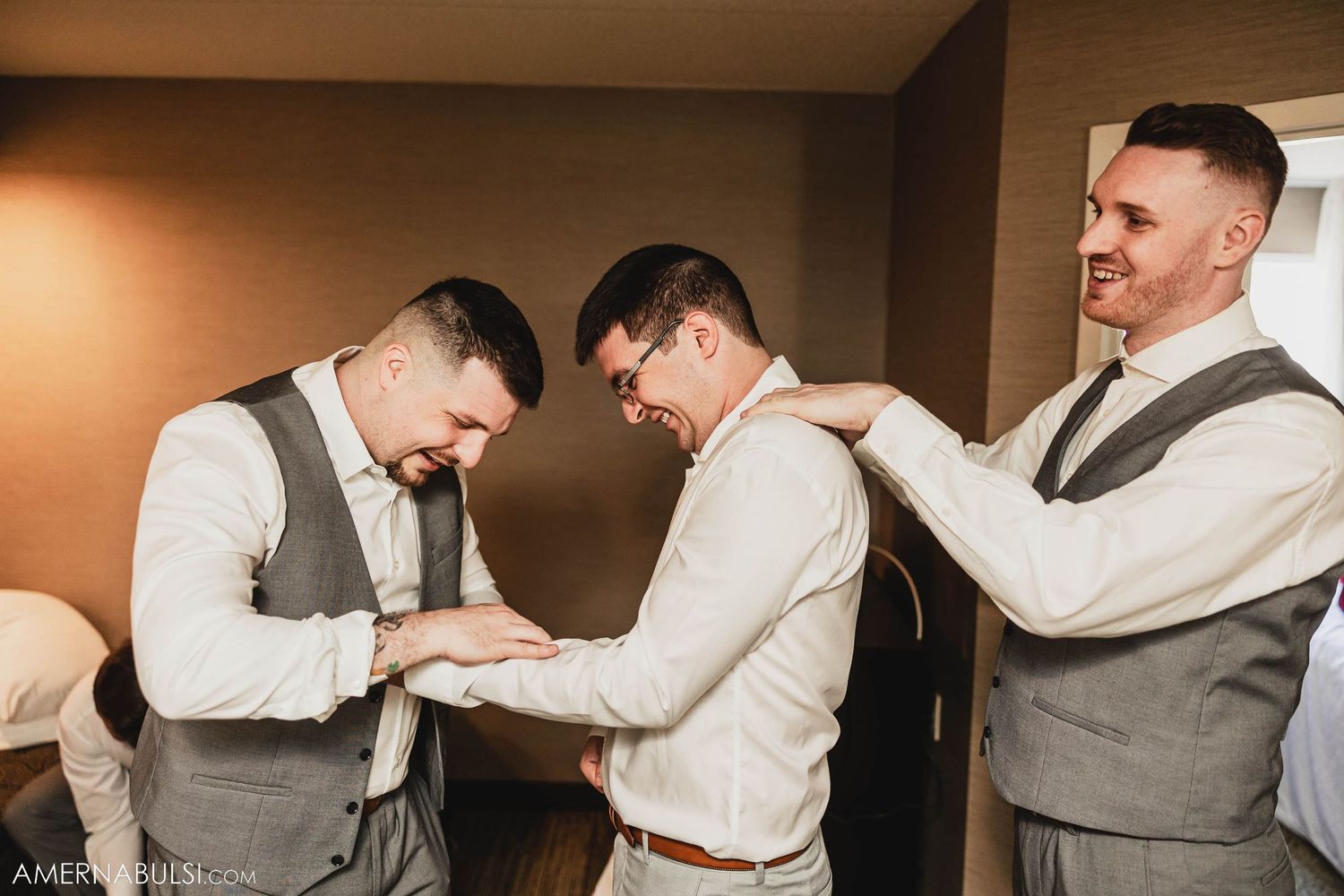 Groomsmen in gray vests and white shirts laughing together during wedding preparations.