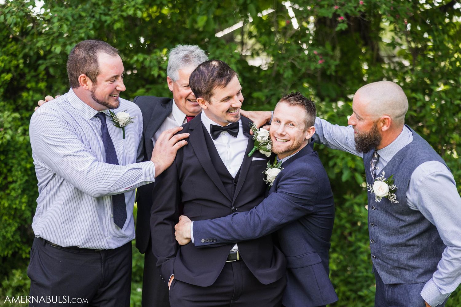Wedding party members playfully posing together in a garden setting.