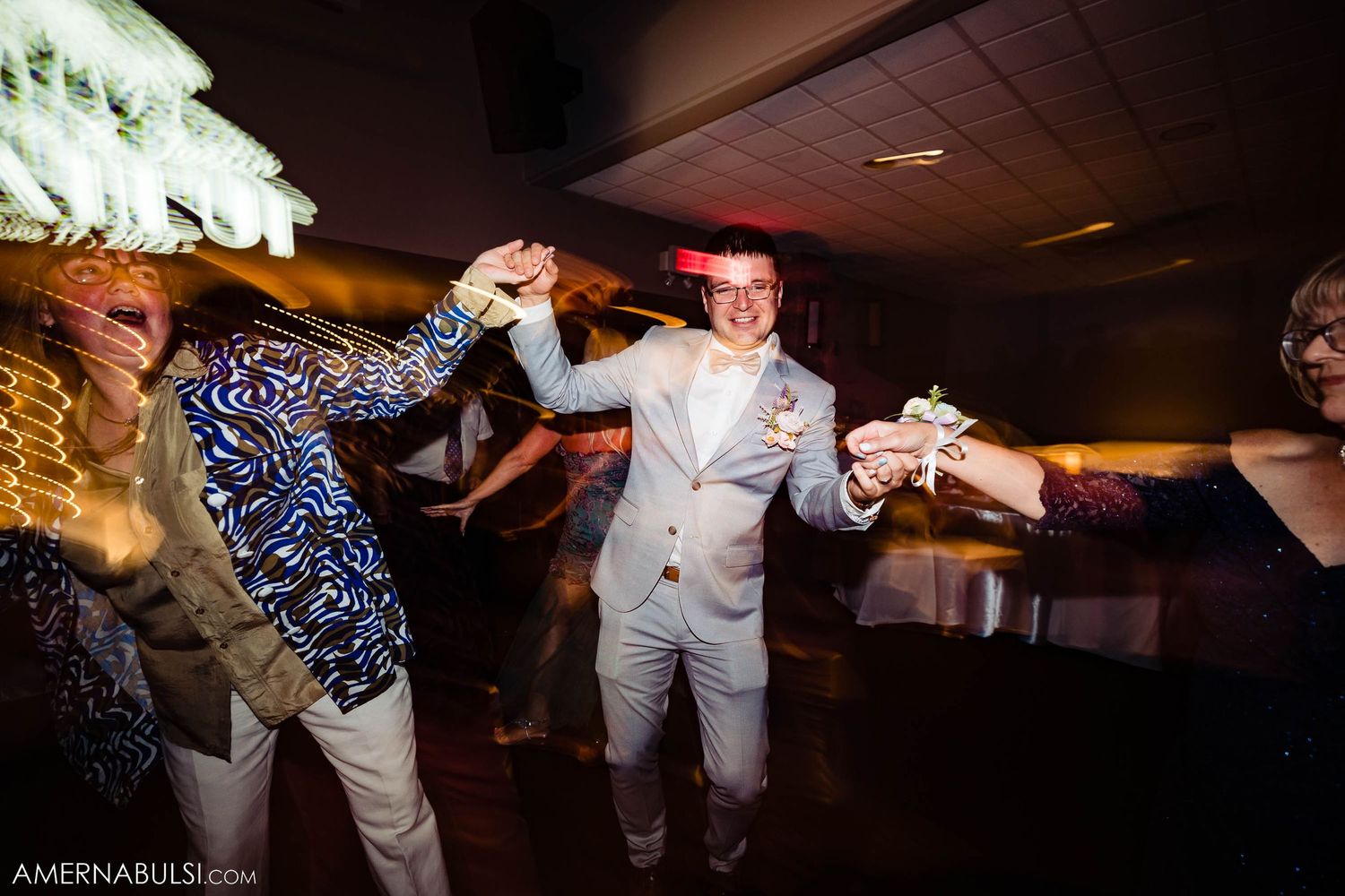 Guests dancing energetically at a wedding reception with festive lighting and decor.