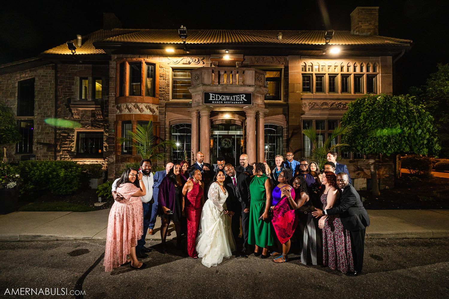 Wedding party group photo outside historic building at night.