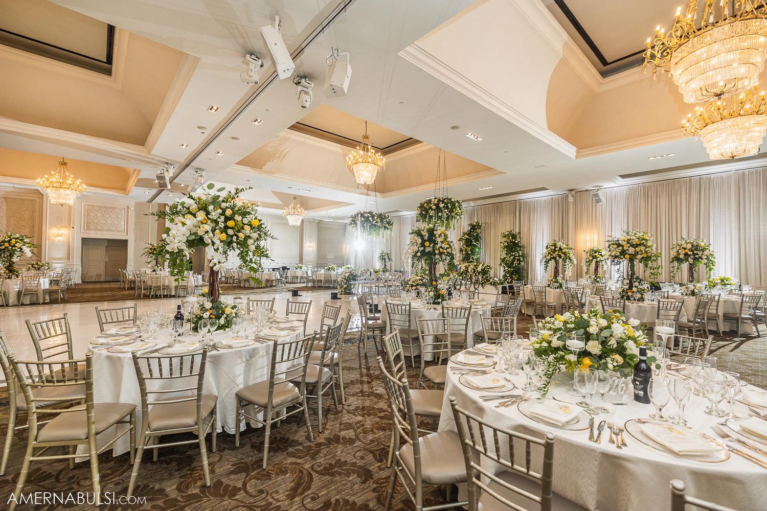 Wedding reception ballroom with round tables, silver chiavari chairs, and elegant floral centerpieces.