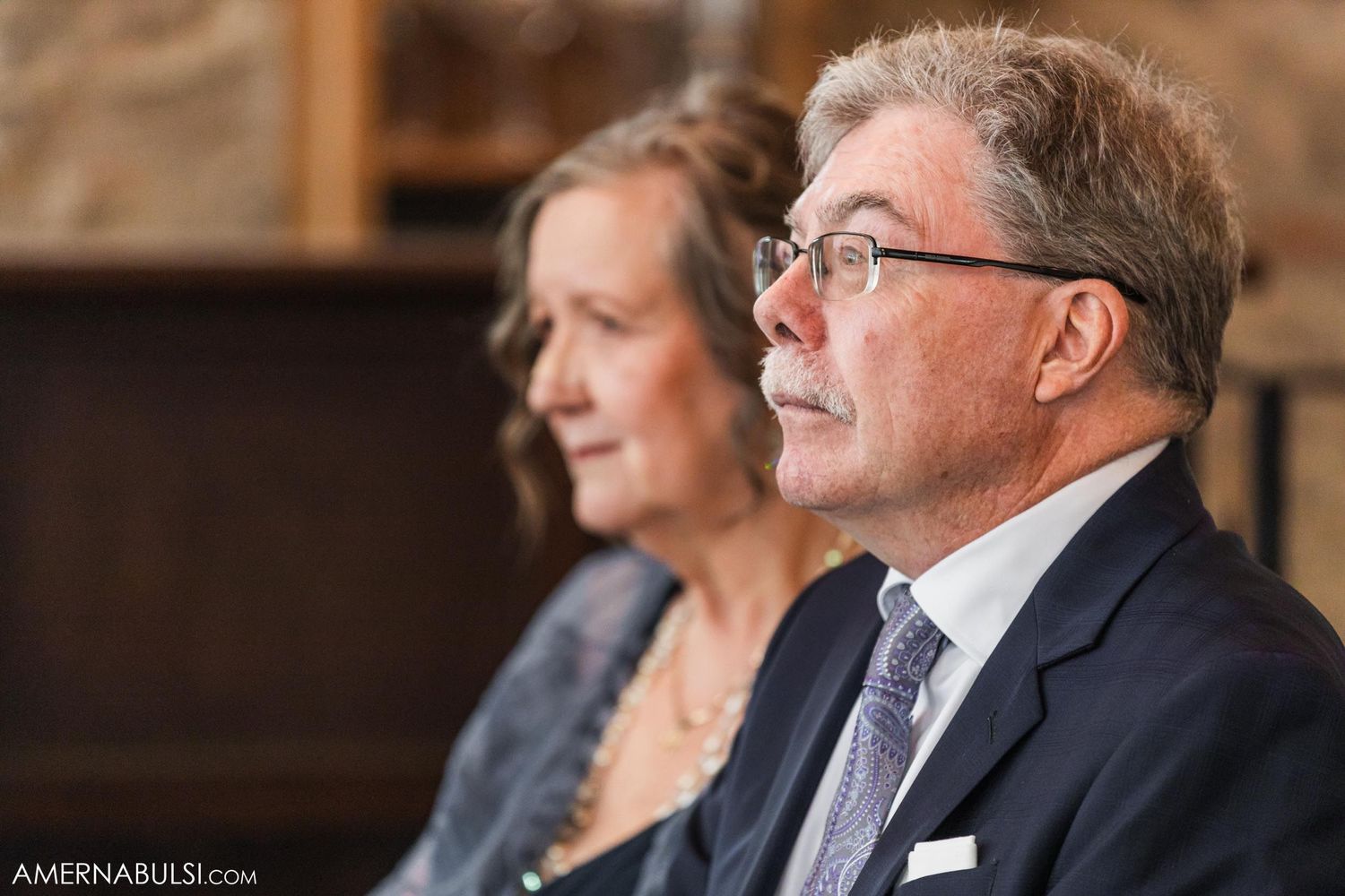 Two guests watching attentively during an indoor wedding ceremony.
