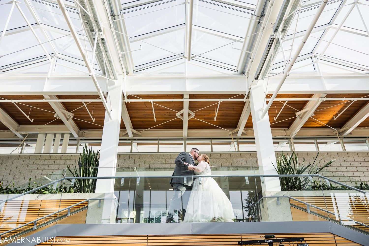 An aerial view of a couple dancing beneath a glass ceiling in a modern wedding venue.