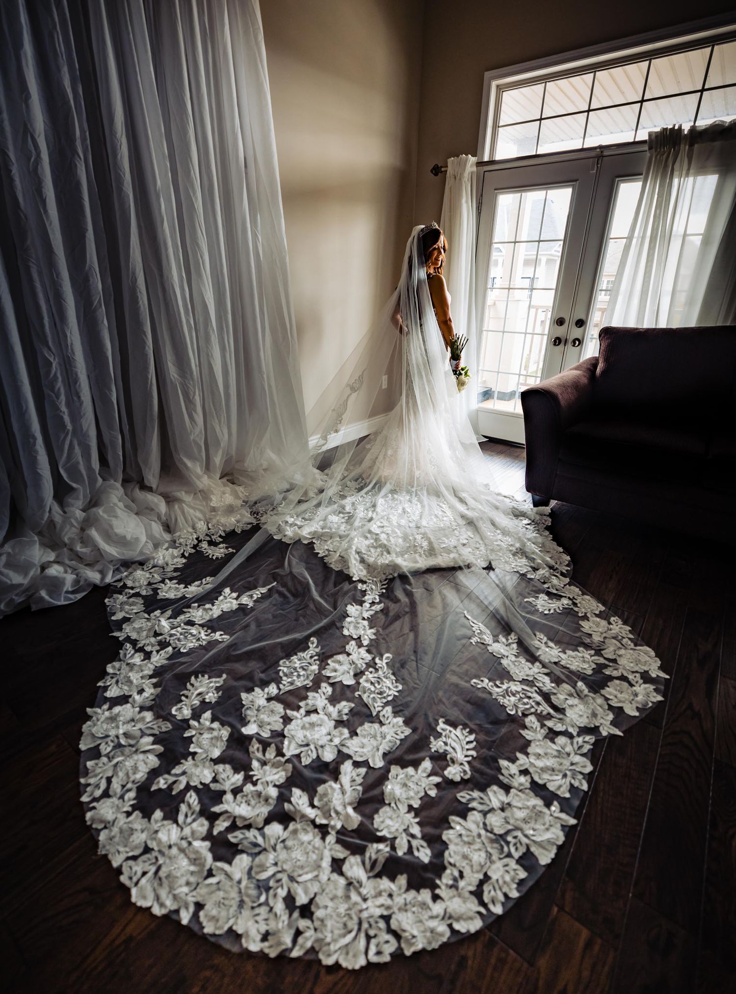 Stunning bridal gown with intricate lace train flowing across dark hardwood floor.