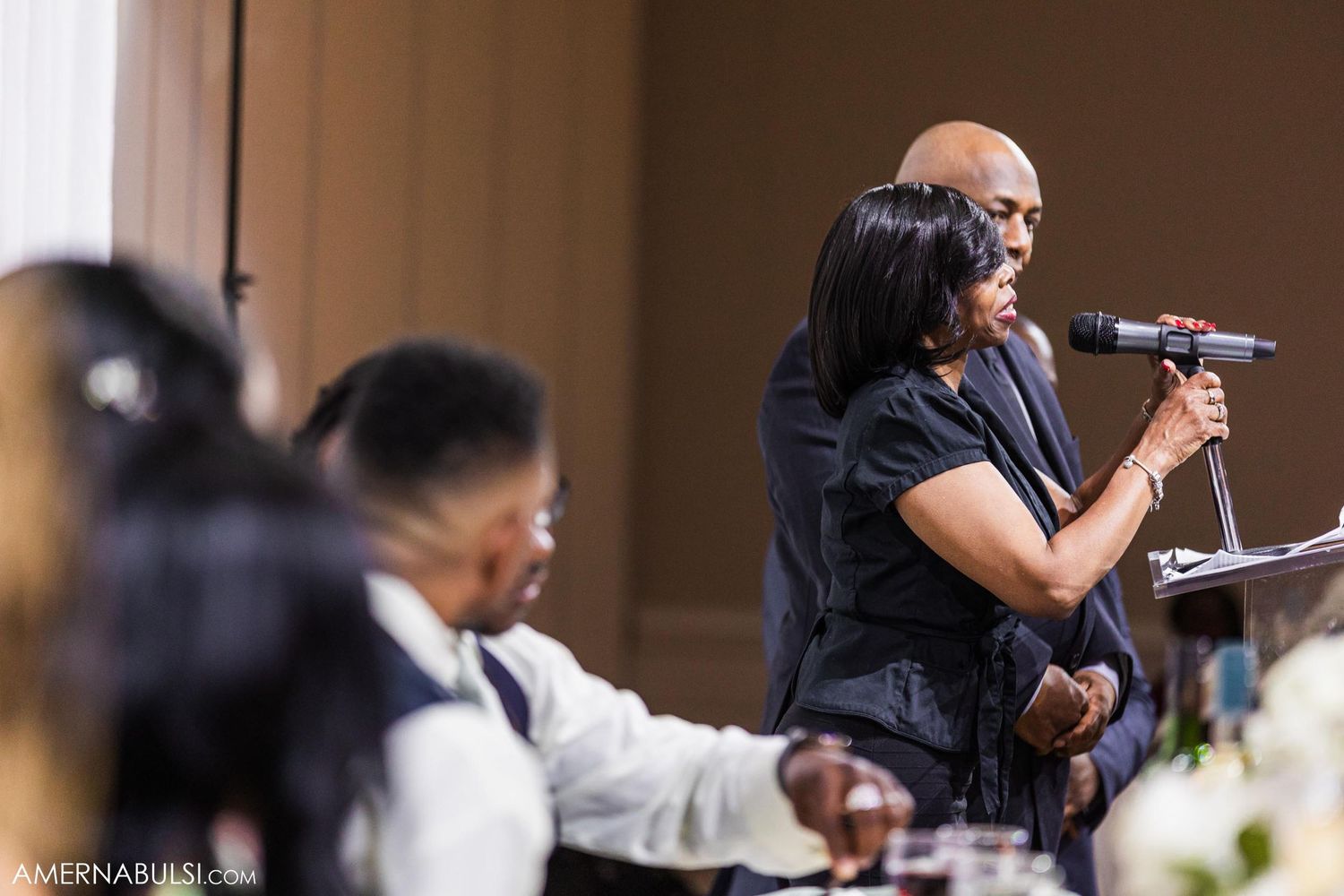 A speaker delivers remarks at a wedding reception using a microphone at an elegant venue.