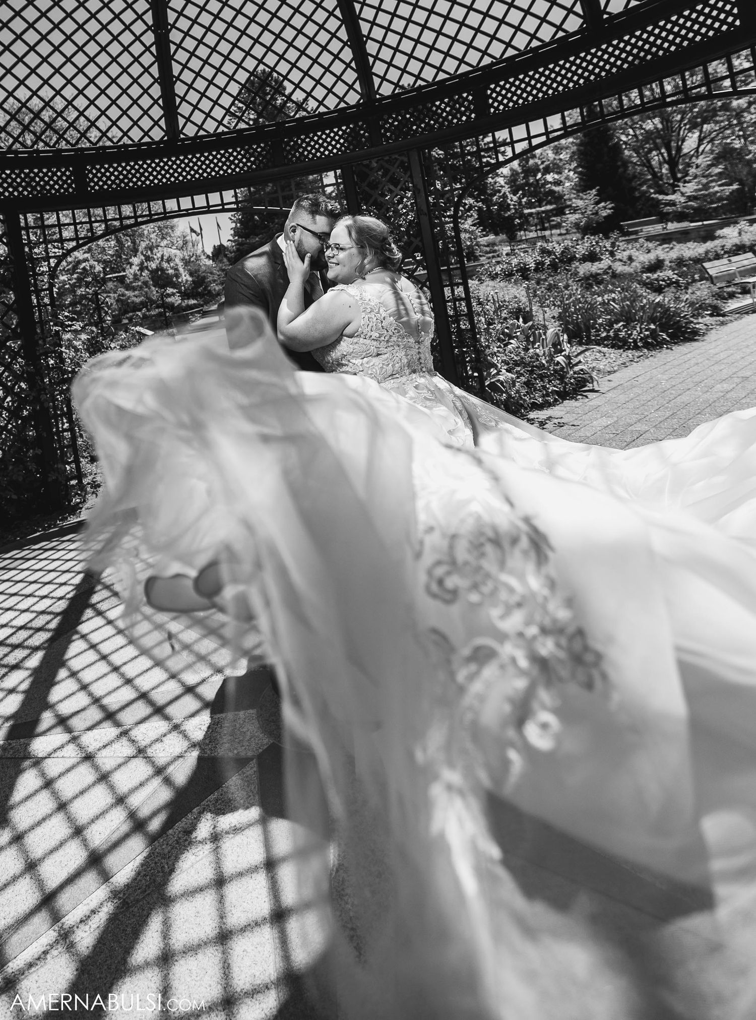 Dramatic black and white wedding photo under latticed gazebo with flowing dress.