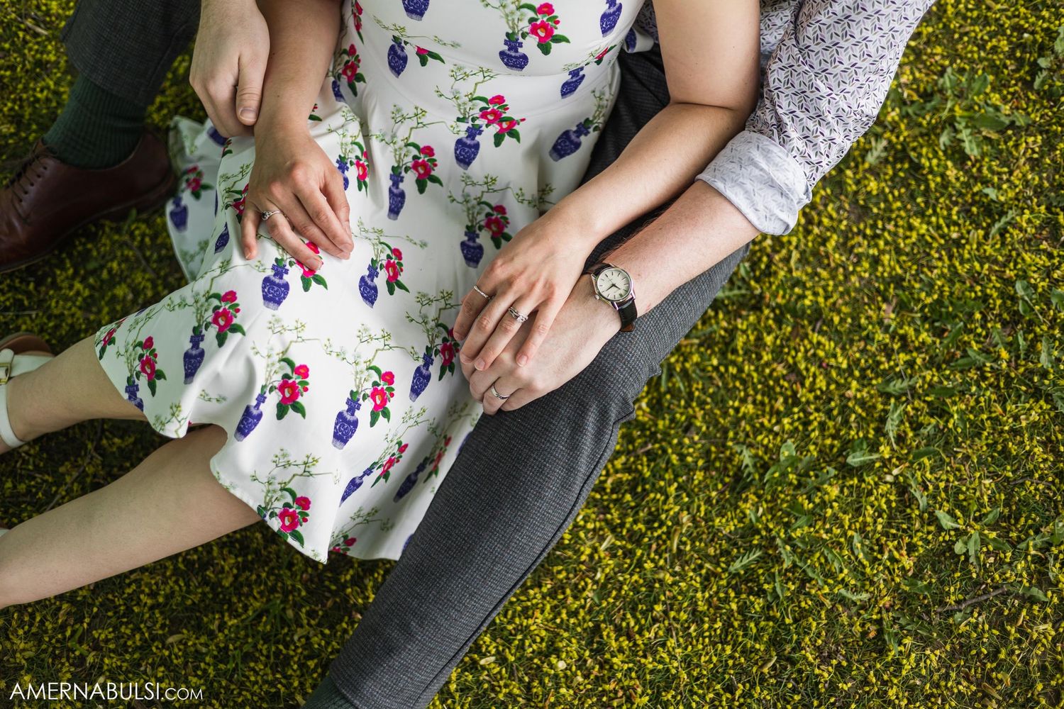 Detail shot of hands and floral dress against lush green grass.