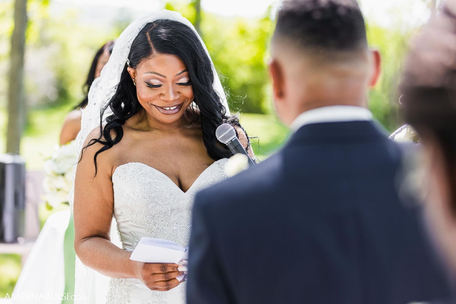 Bride smiling while reading vows during outdoor wedding ceremony.
