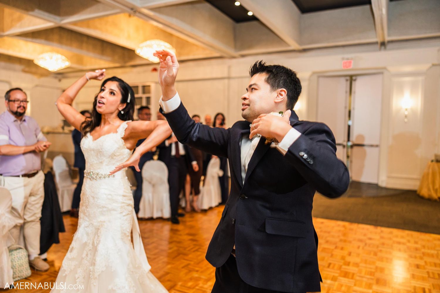 Newlyweds dancing energetically on a wooden dance floor during their wedding reception.