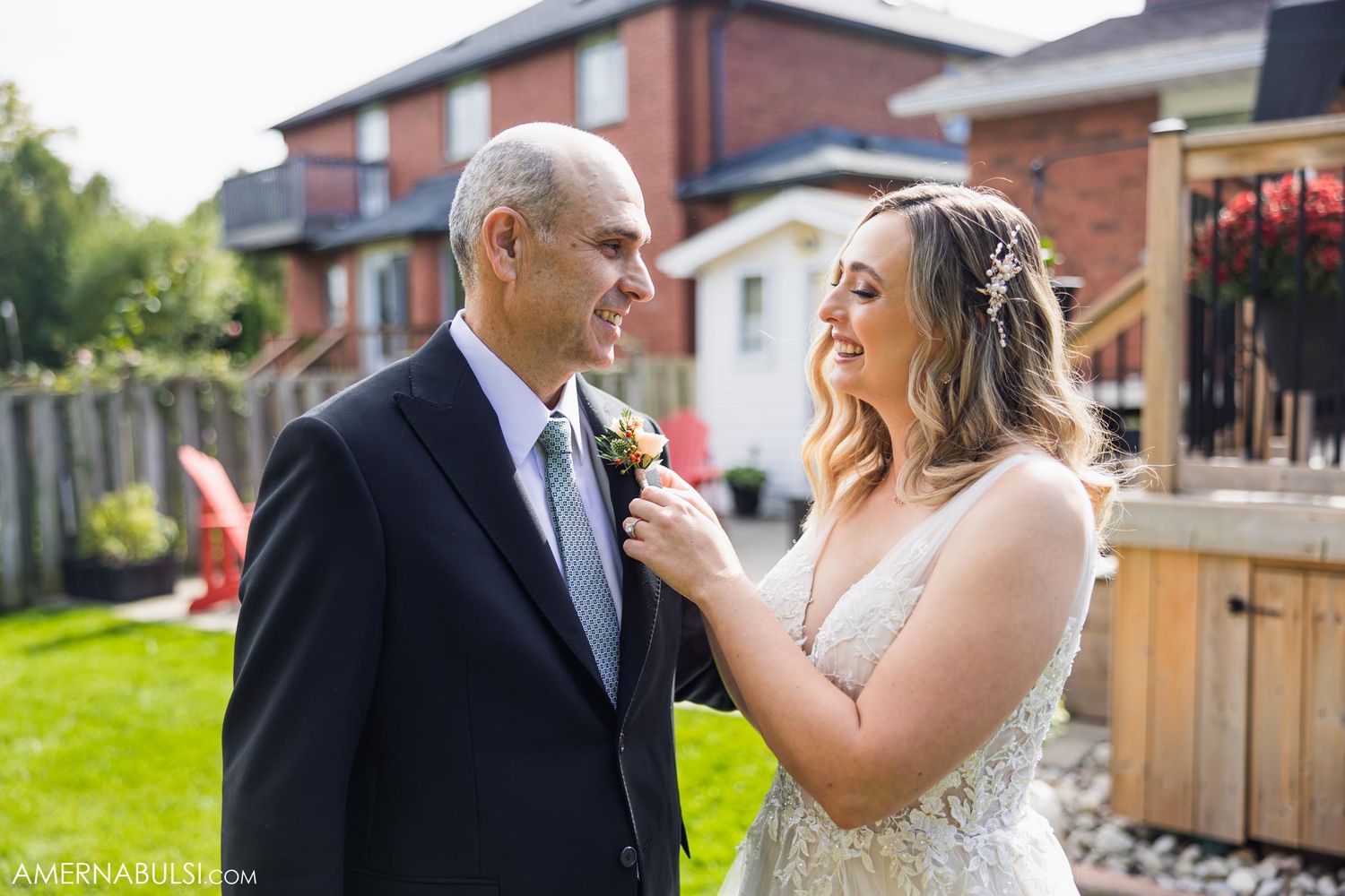 A touching moment between a bride and her companion in formal wedding attire on a backyard deck.