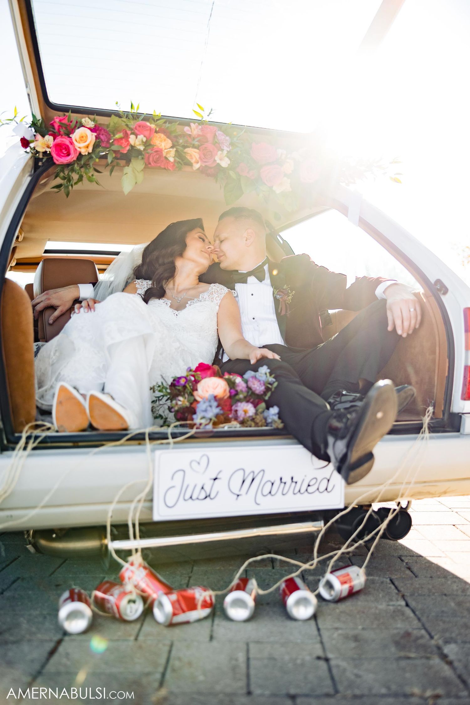 Romantic car trunk portrait with floral decorations and 'Just Married' sign during golden hour.