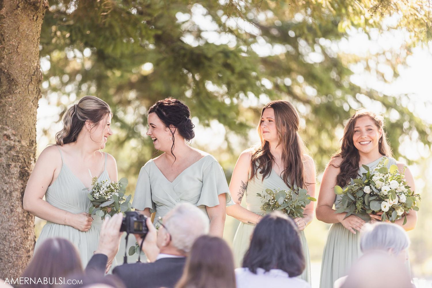 Bridesmaids in soft mint dresses share joyful moments during an outdoor wedding ceremony.