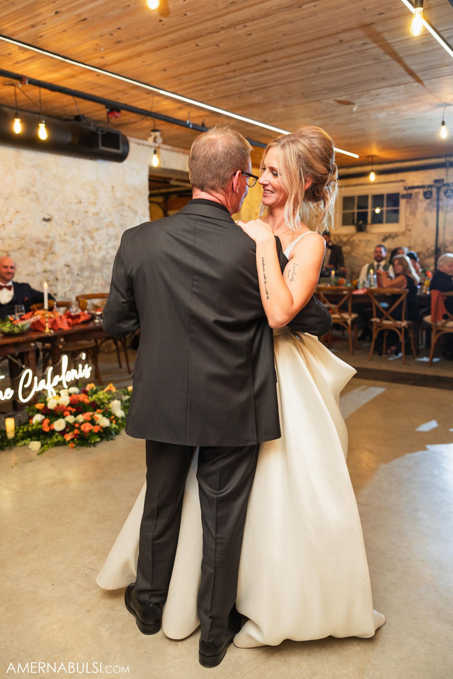 Romantic first dance moment in a rustic indoor venue with string lights.