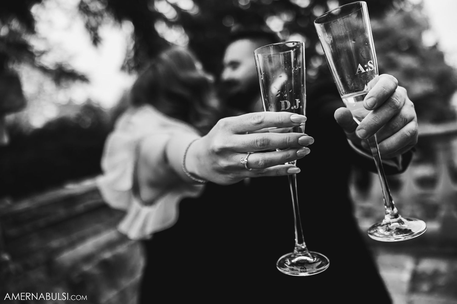 Two hands hold champagne glasses together in a celebratory toast, captured in black and white.