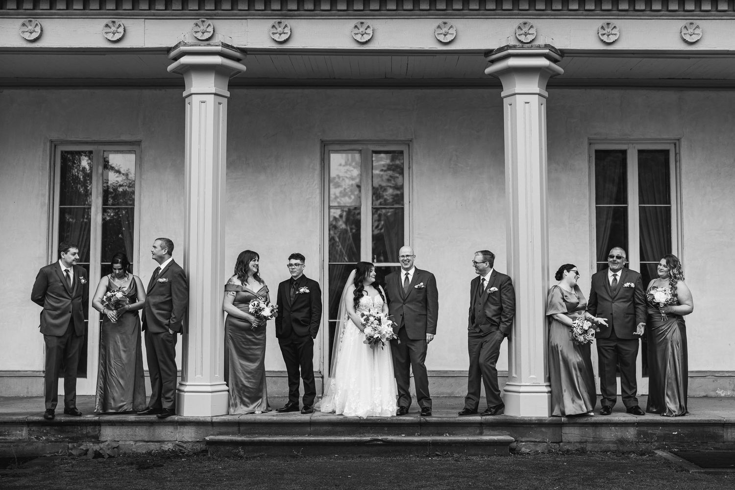 Black and white photo of wedding party lined up on mansion's columned porch.