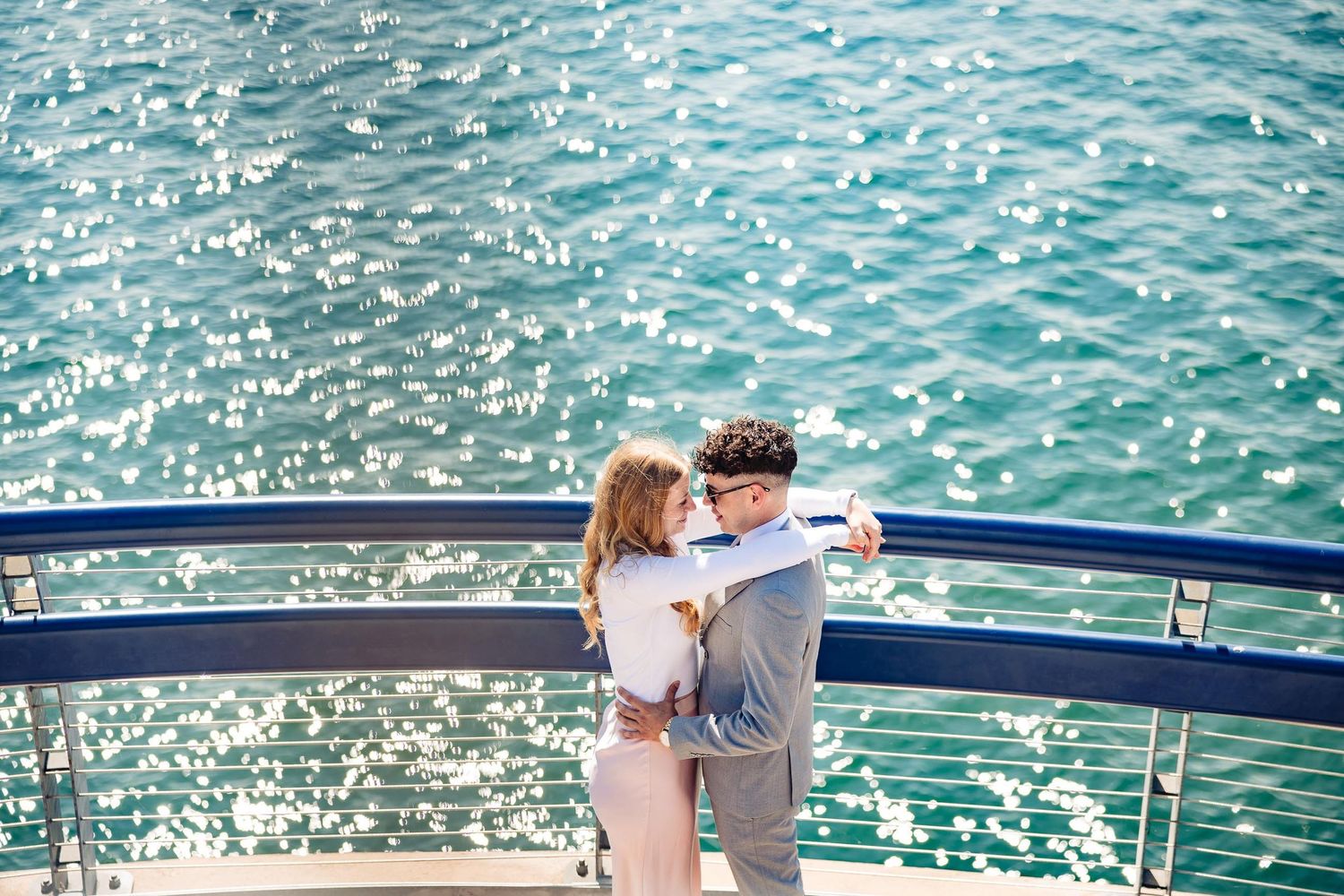 Couple embracing on cruise ship deck with sparkling ocean water background.