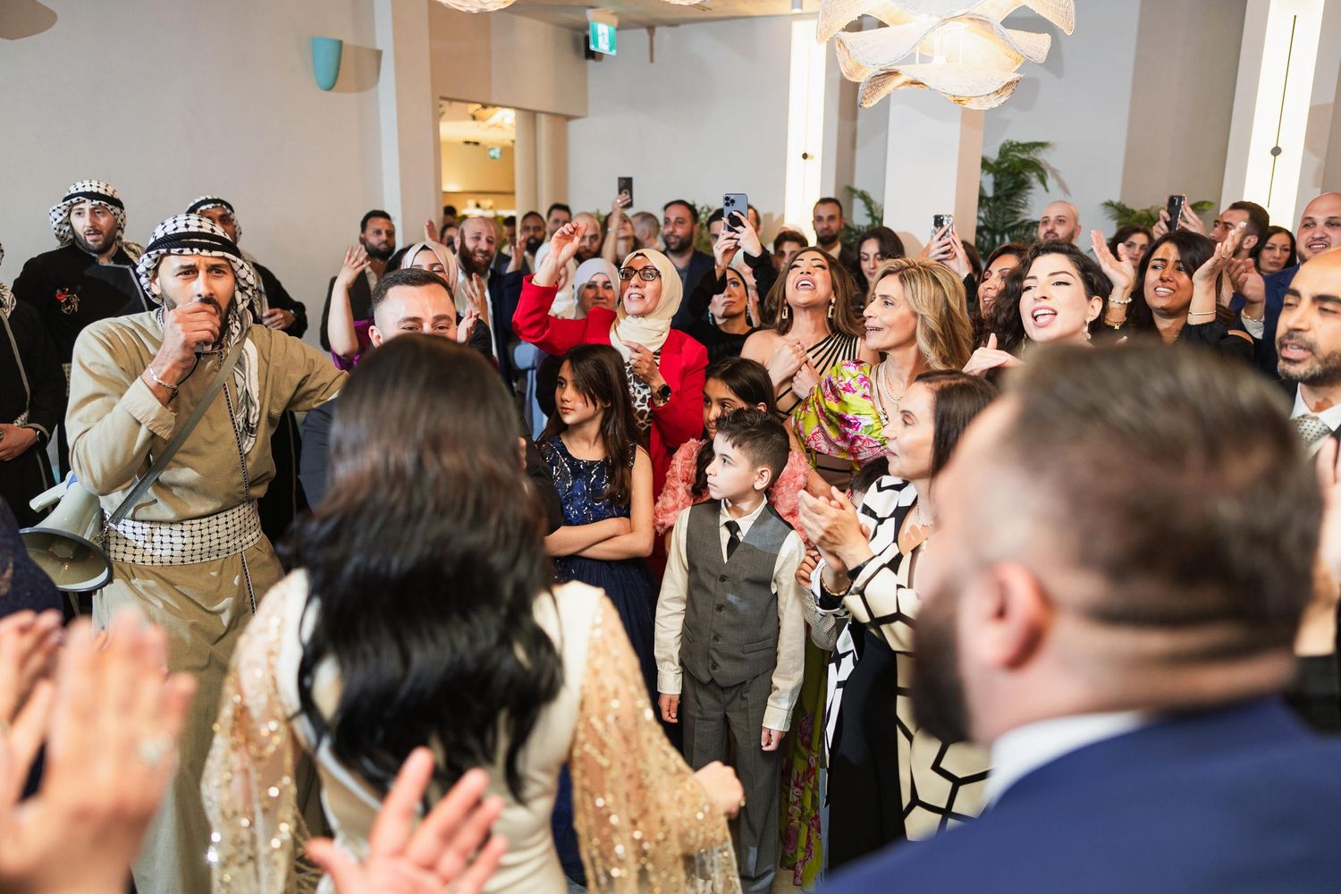 Wedding guests cheering and clapping during a celebration in an elegant indoor venue.