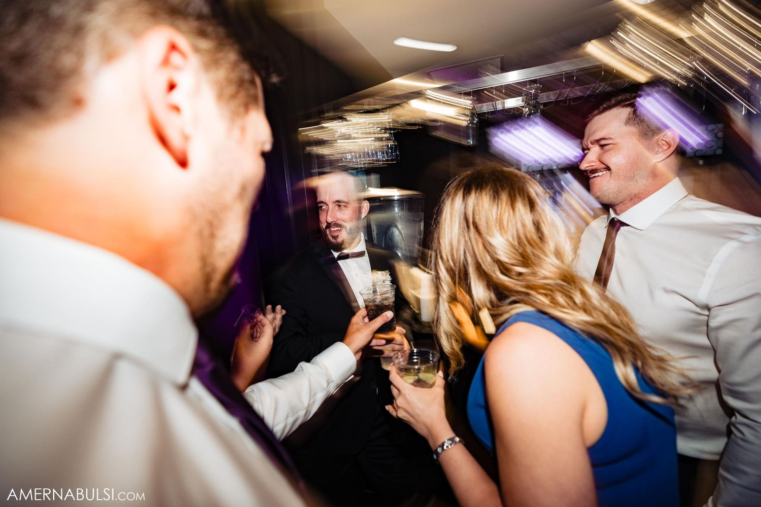 Wedding reception dance party with colorful lighting and guests celebrating.