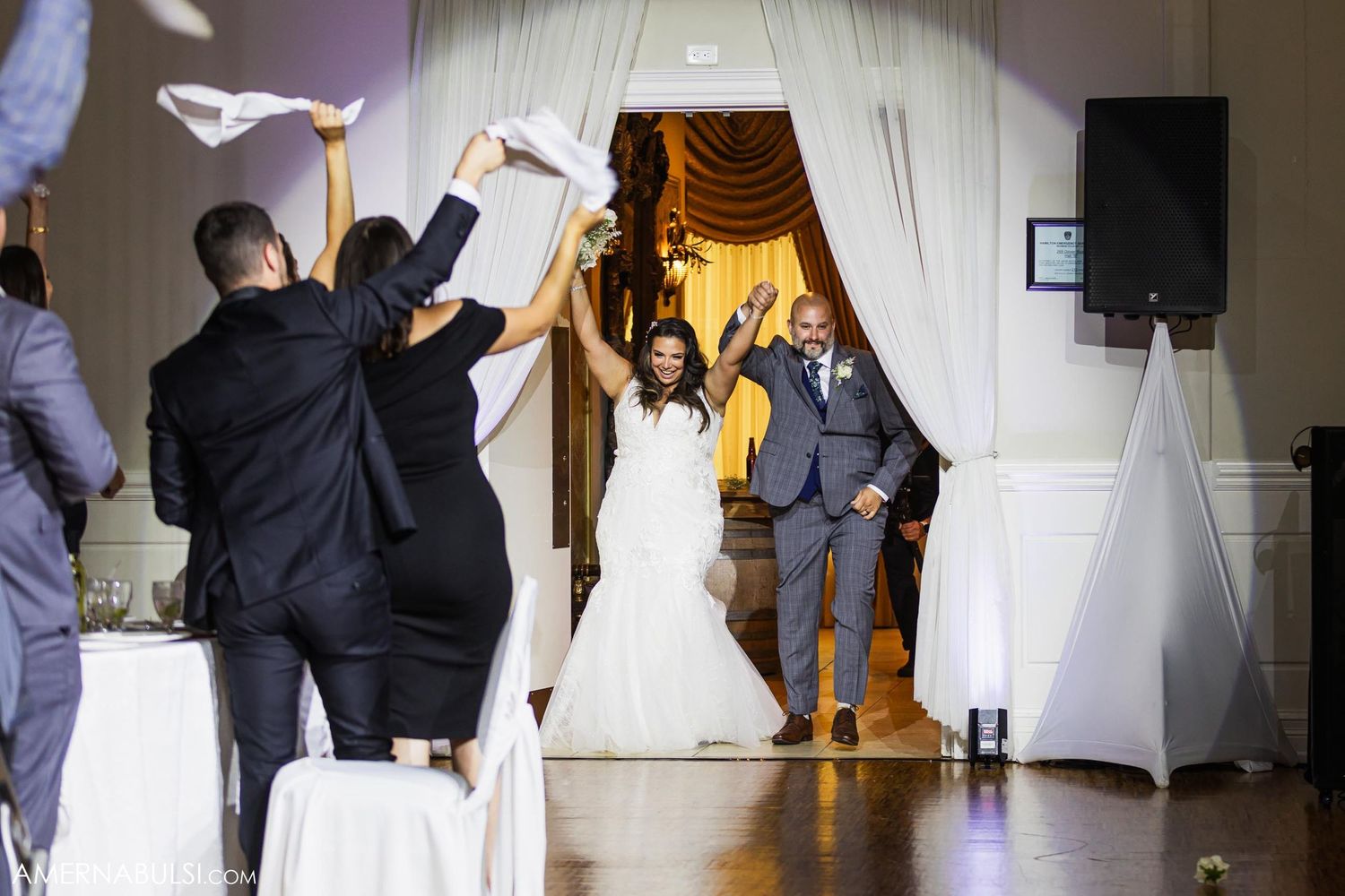 Wedding party entrance through white fabric doorway with celebratory gestures and raised arms.