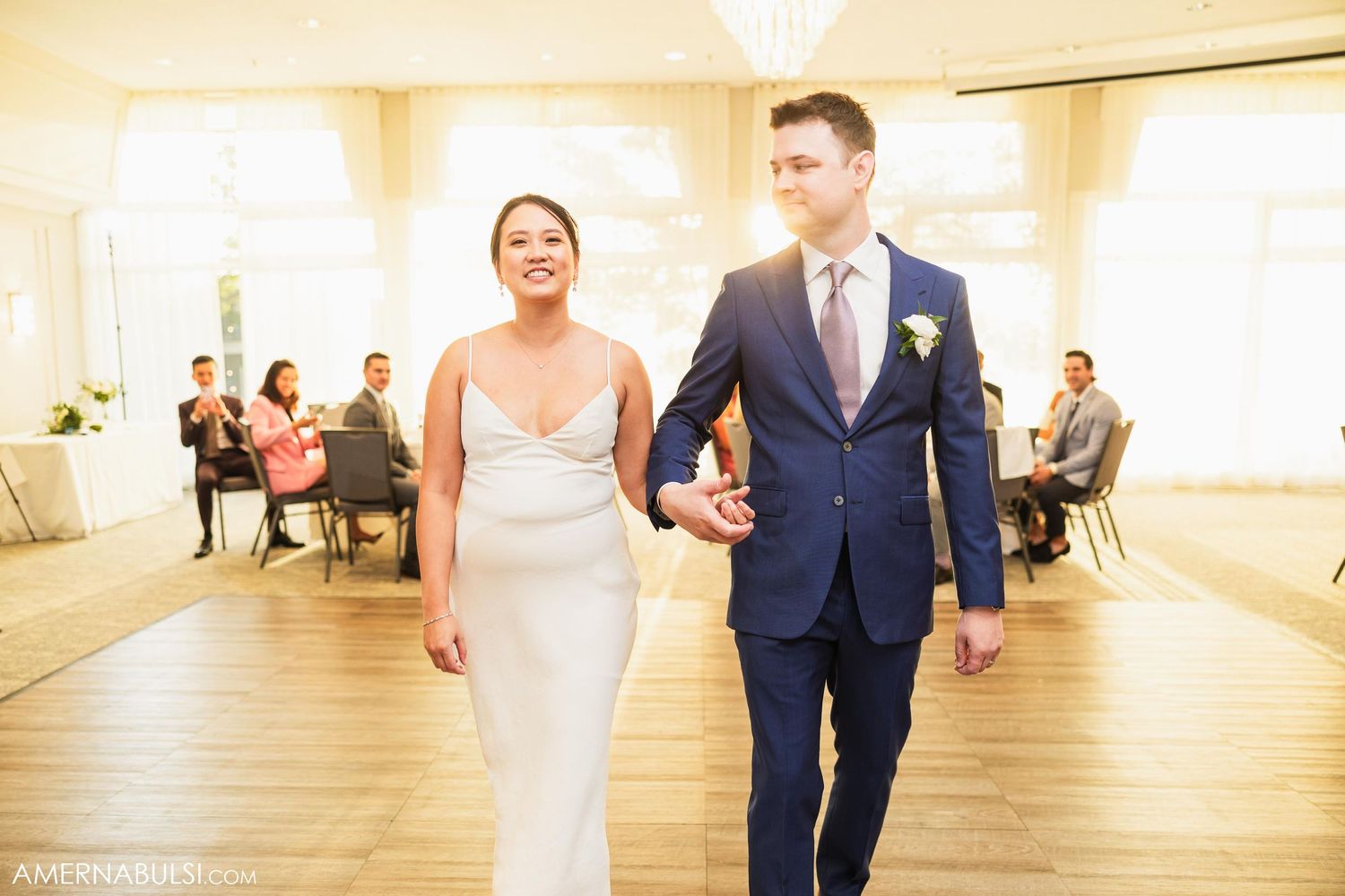 Newlyweds walk arm in arm across the ballroom floor during their wedding celebration.