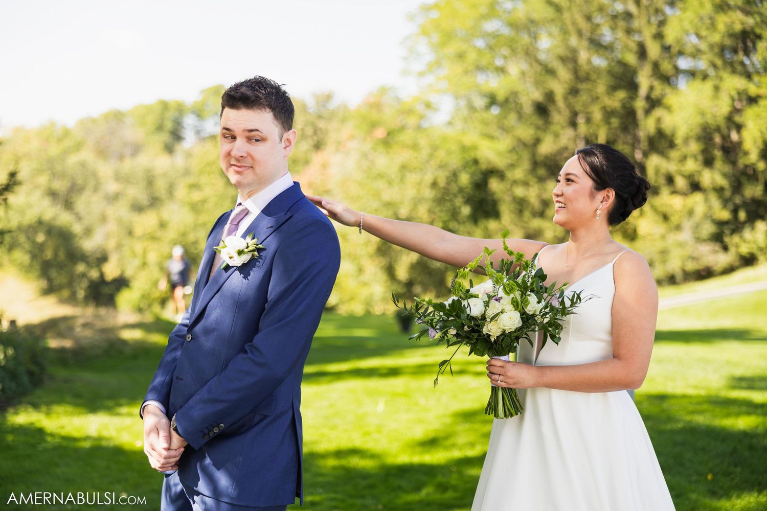 Playful wedding portrait of couple on sunny lawn with bride tapping groom's shoulder.