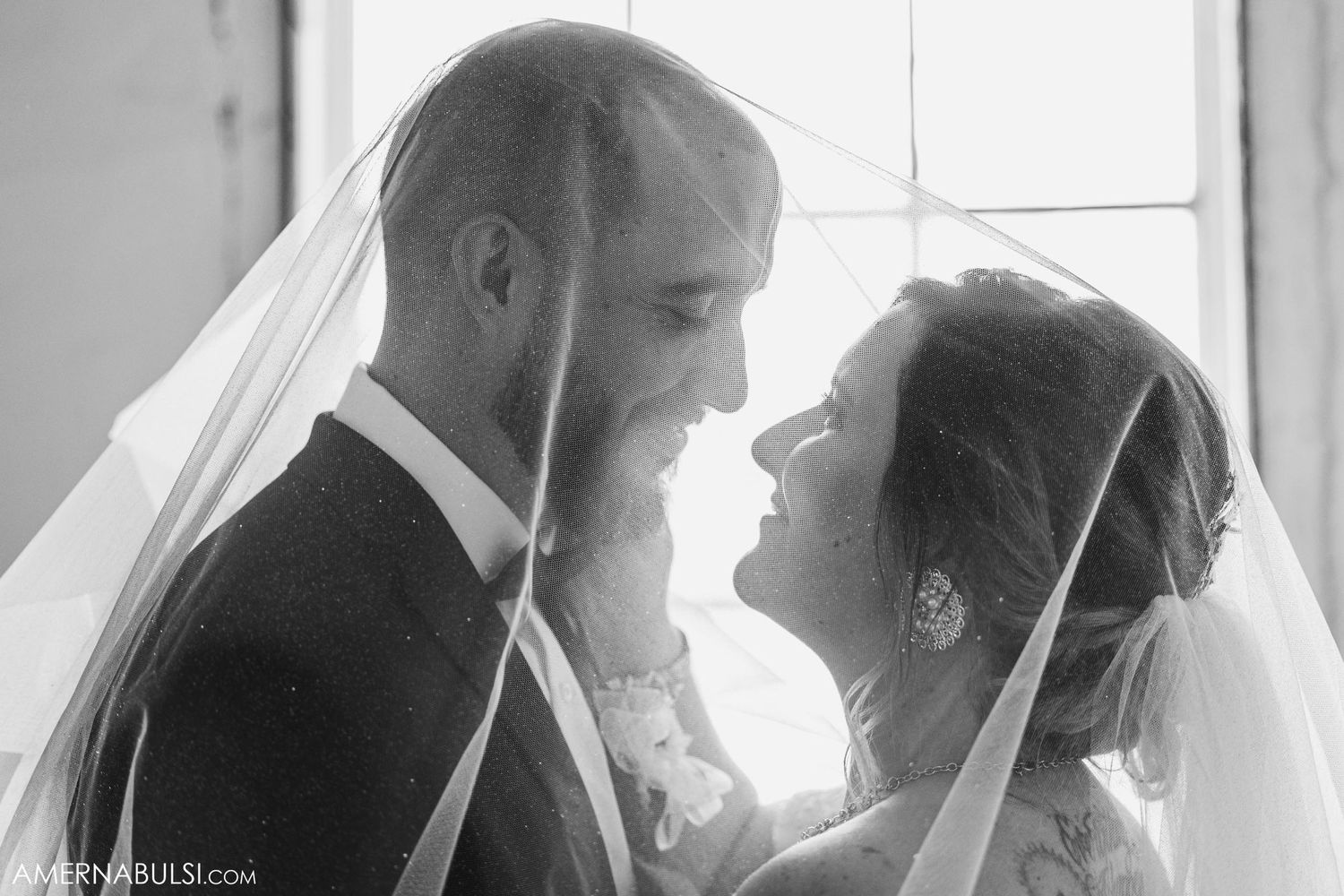 Intimate black and white wedding portrait with flowing veil and natural window light.