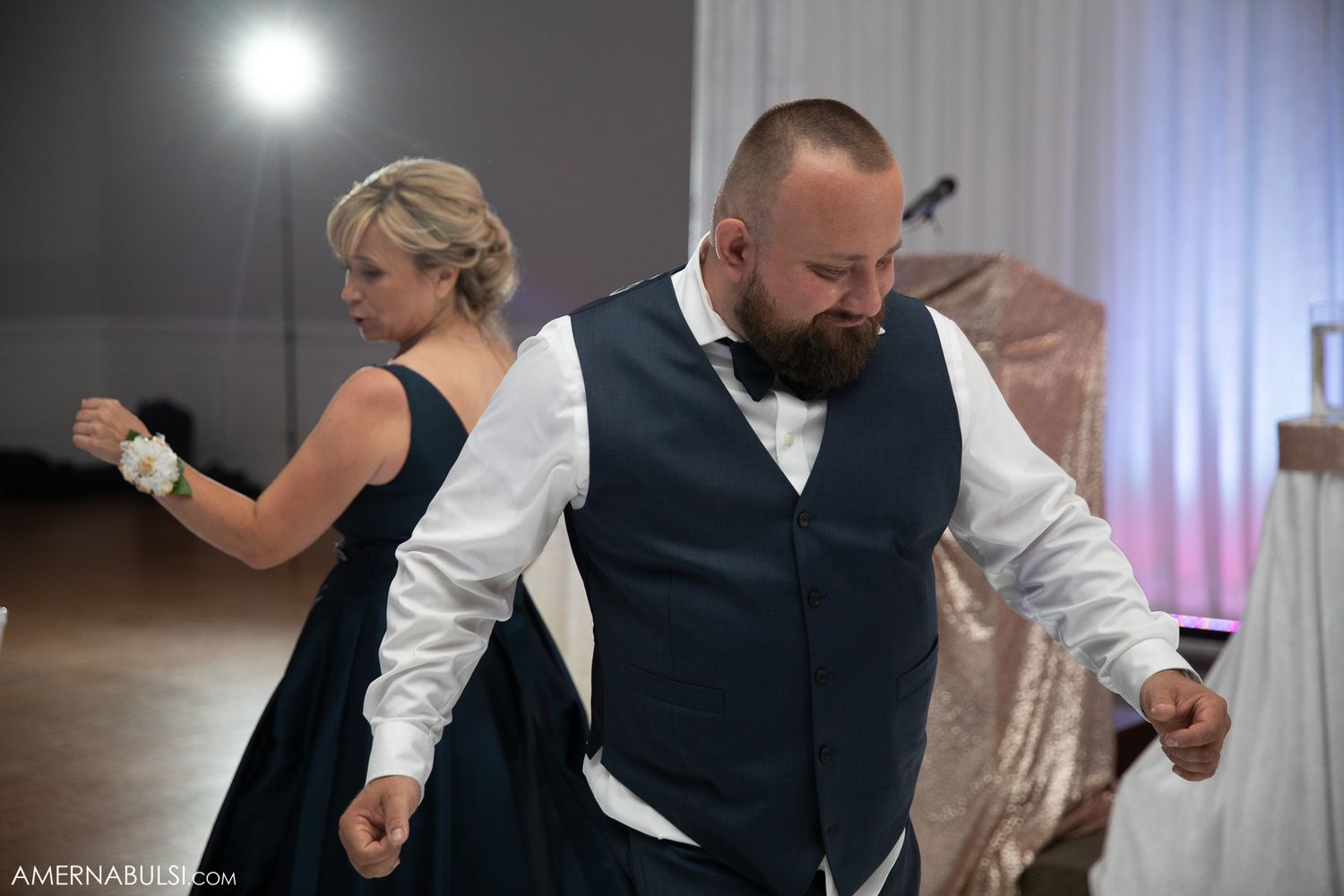 Guests dancing energetically at a wedding reception in a ballroom with dramatic lighting.
