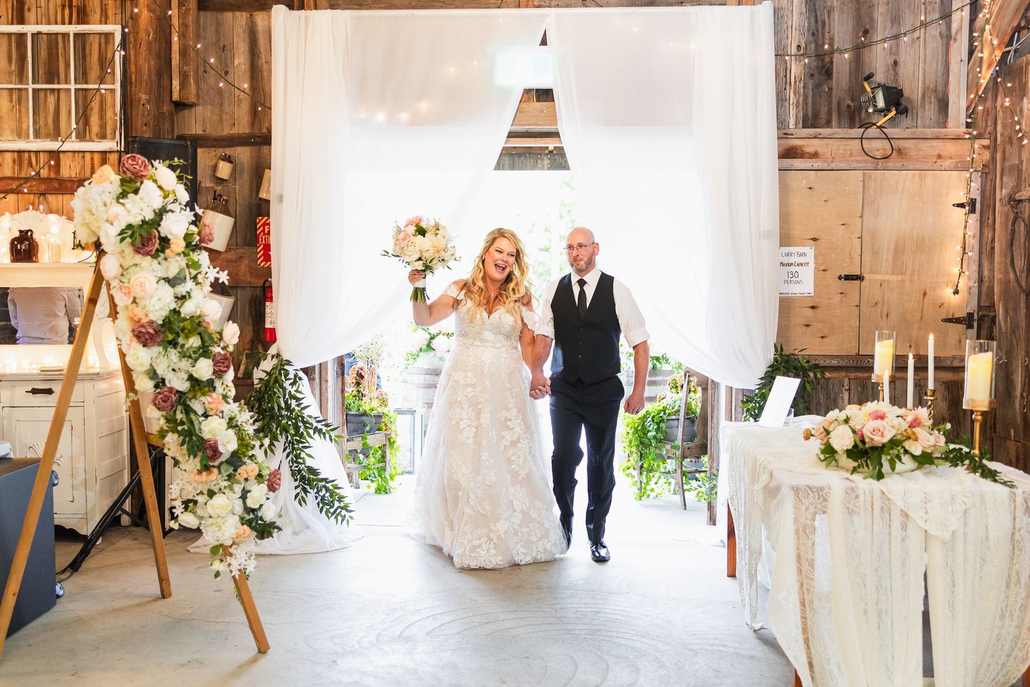 Rustic barn wedding venue decorated with white drapes, flowers and wooden accents.