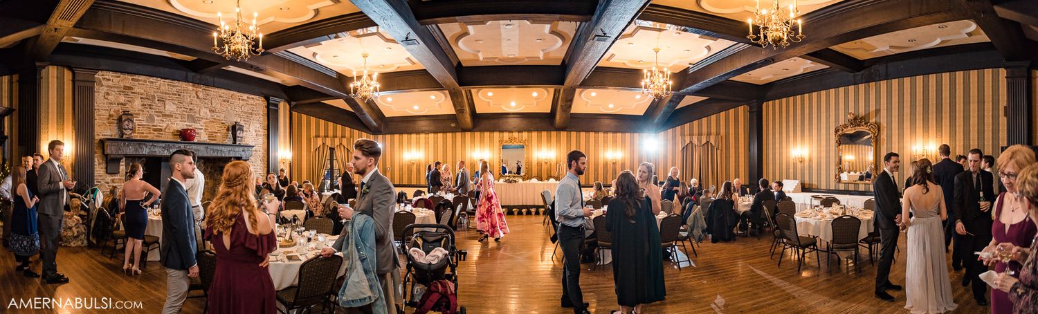 Panoramic view of a luxurious wedding reception hall with wooden beams and warm lighting.