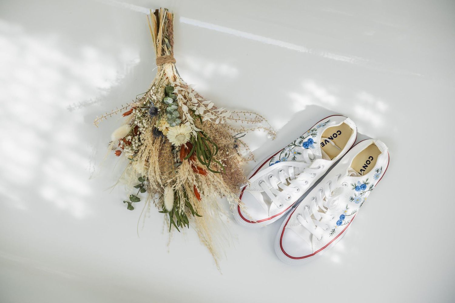 Dried flower bouquet hanging beside white canvas sneakers with floral details.
