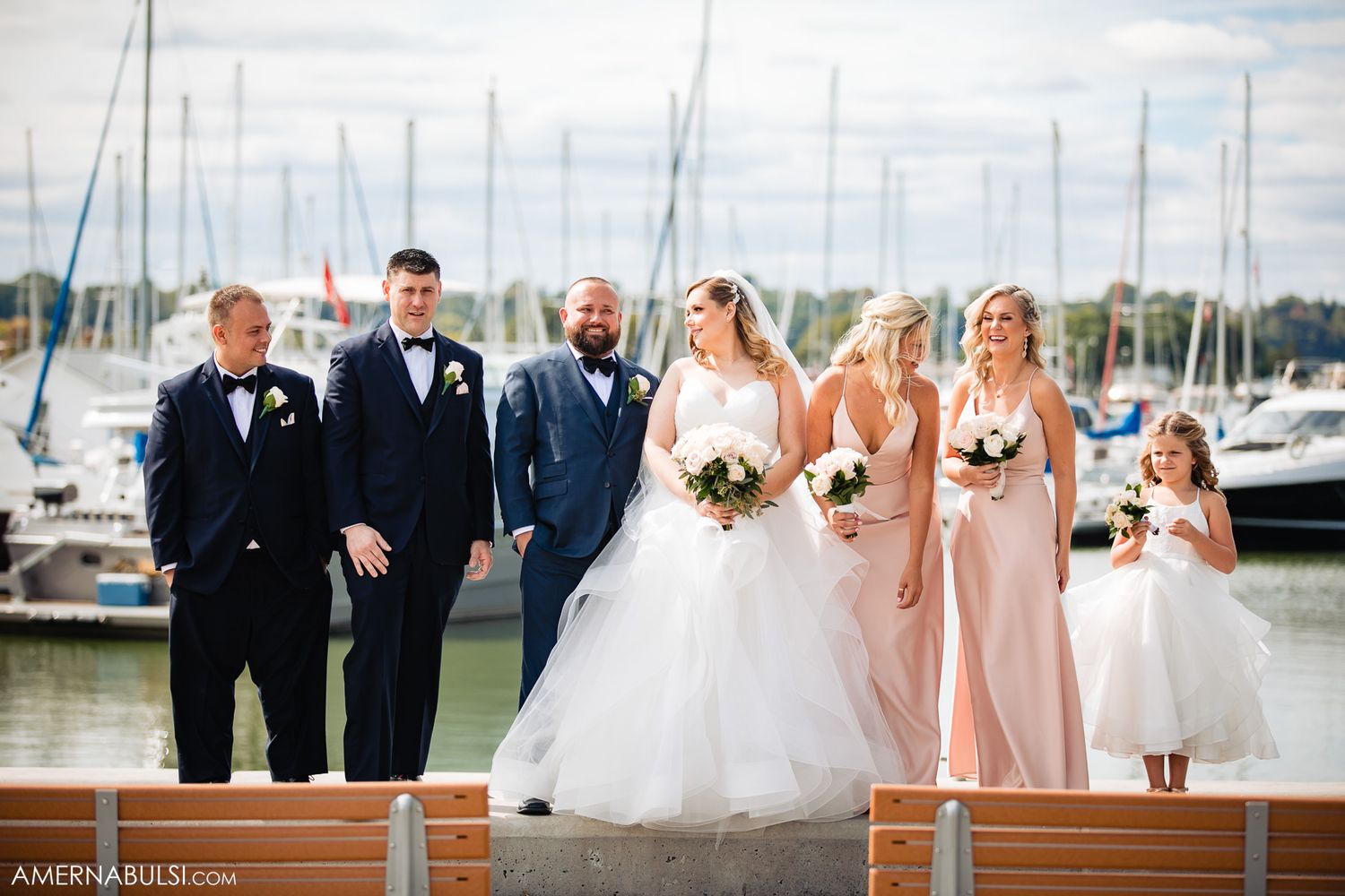 Wedding party posing at a marina with boats and docks in the background.