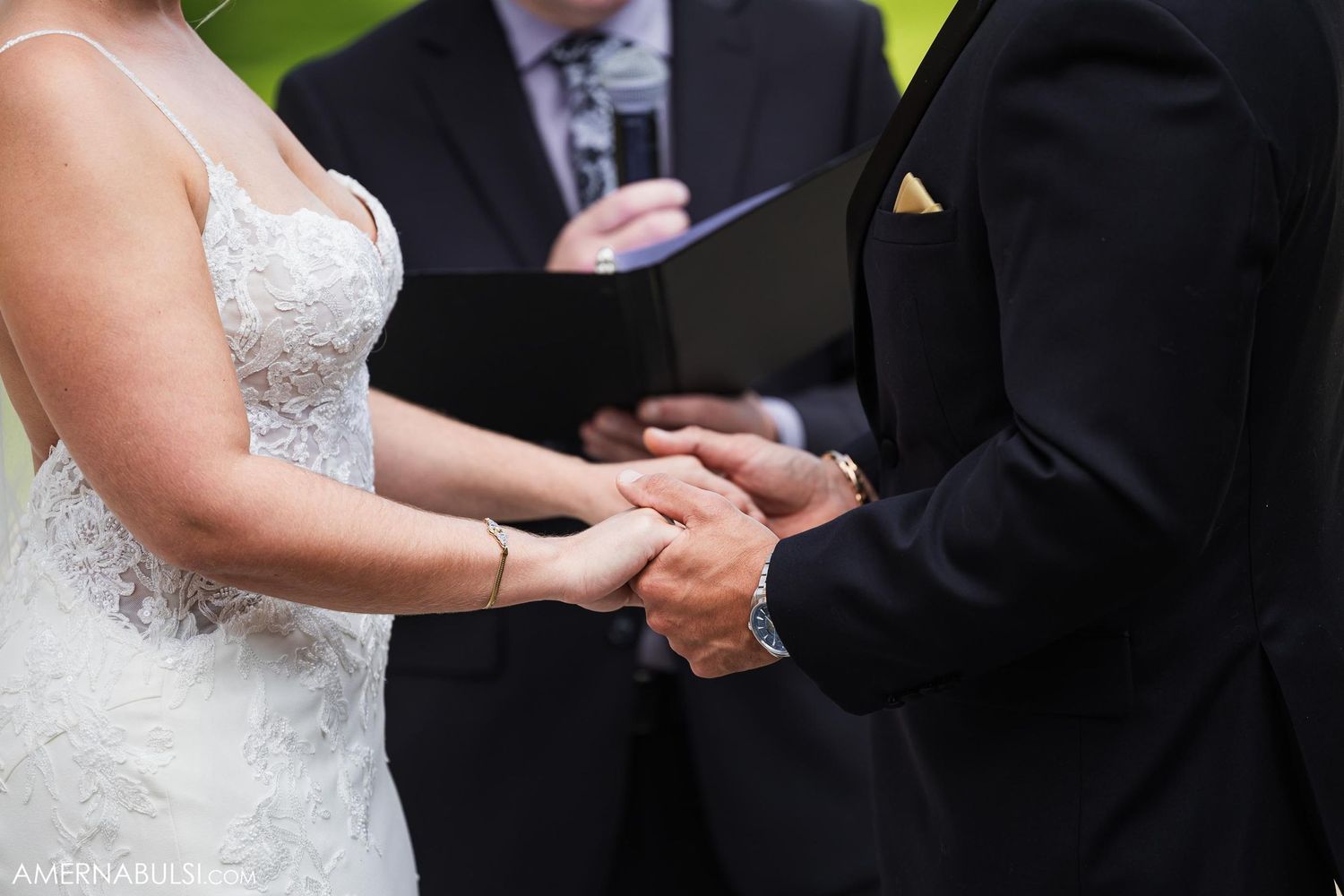 Close-up of hands clasped during wedding ceremony vow exchange.