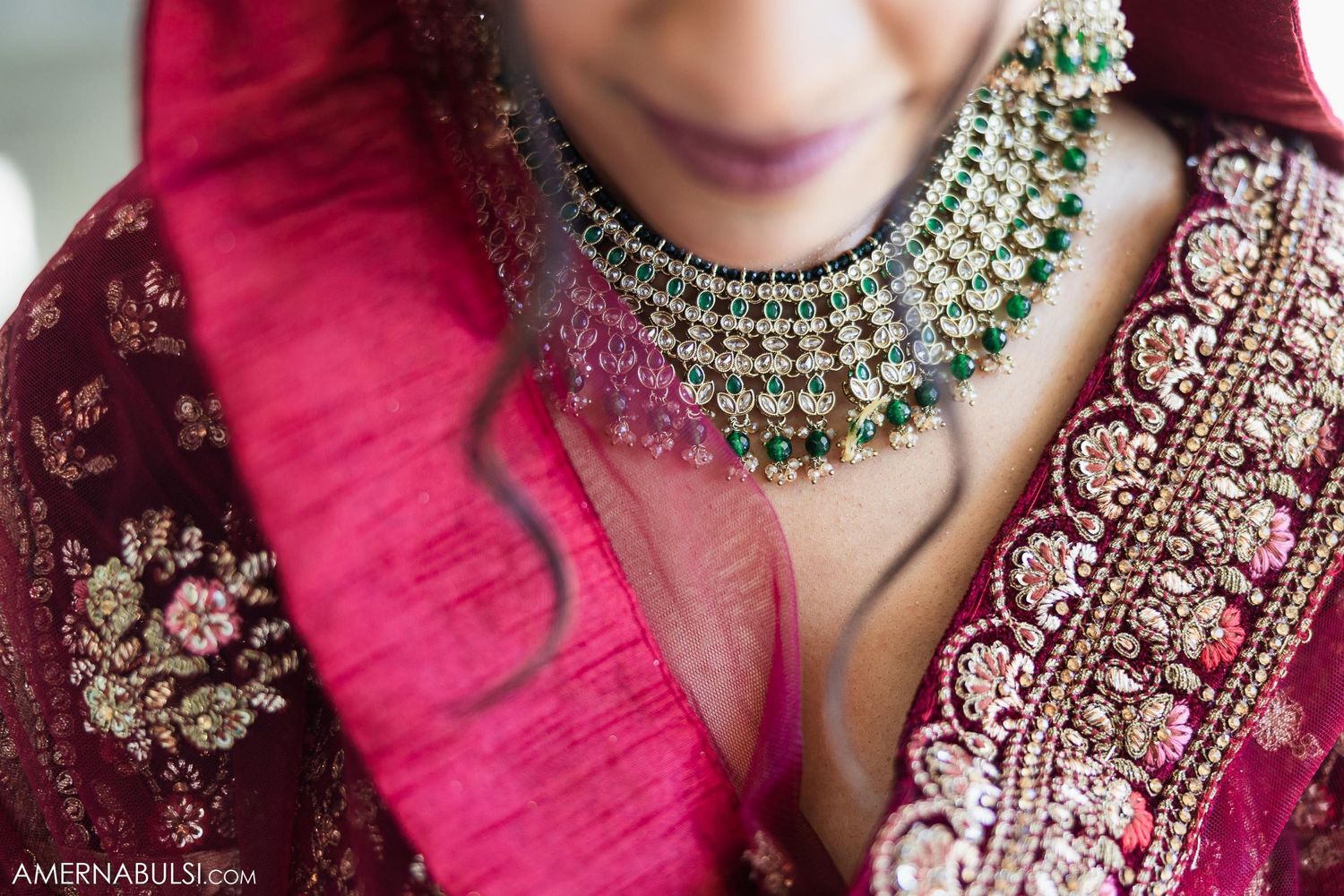 Close-up of an ornate green and gold kundan necklace worn with red and embroidered wedding attire.